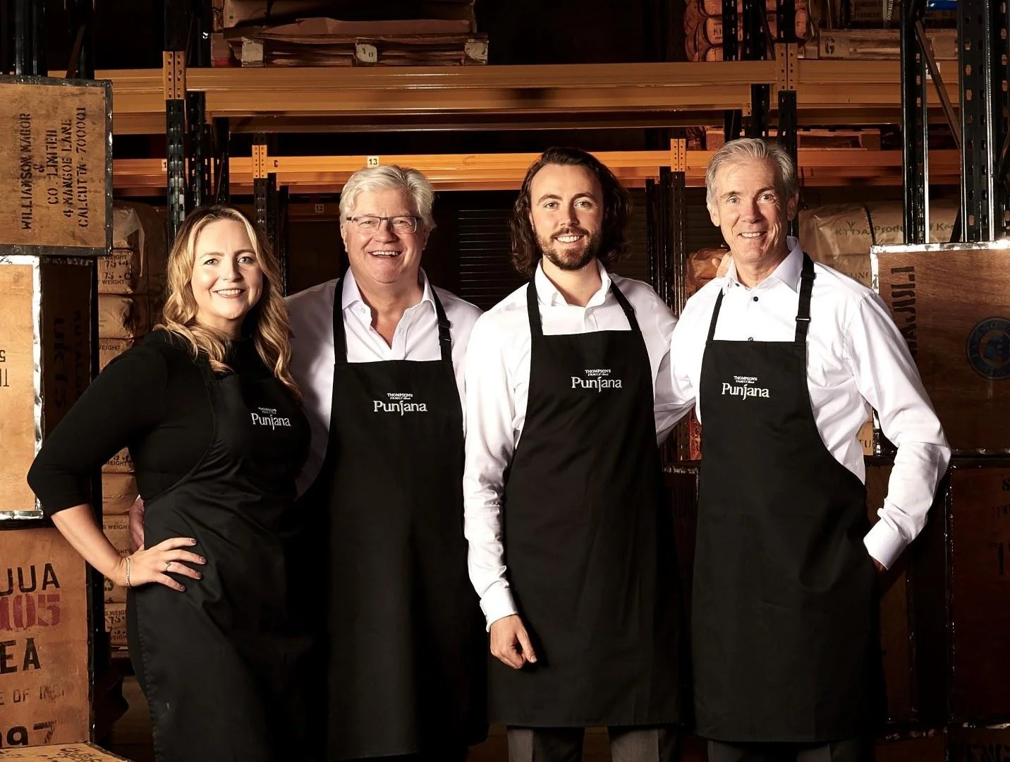 Group of five people standing in a warehouse wearing black aprons with 'Punjab' written on them, smiling at the camera.