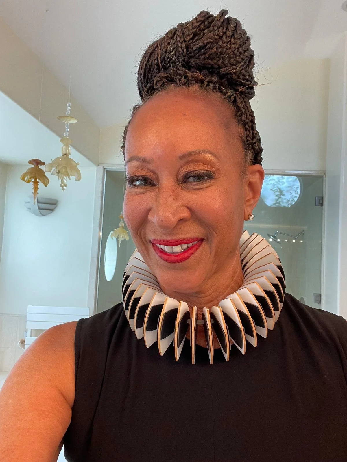 A woman with styled braids wearing a large, geometric black and white collar necklace smiling.