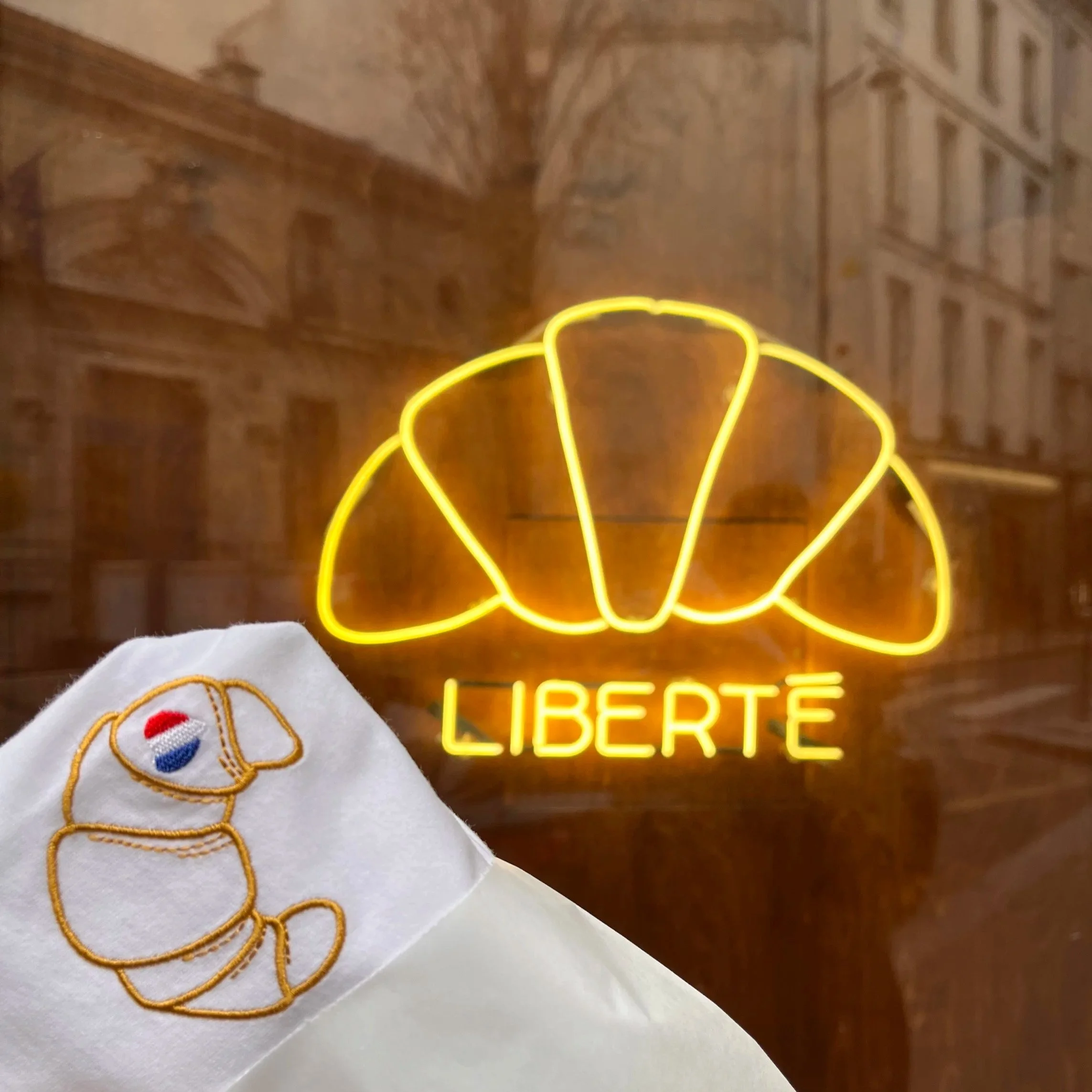 Un t-shirt brodé d'un croissant, vendu dans un emballage de croissant au sein de la boulangerie LIBERTÉ à Paris. Une création à l'image de la créativité et la qualité des produits de l'agence l'OVERALL de Eva Bromerg. 