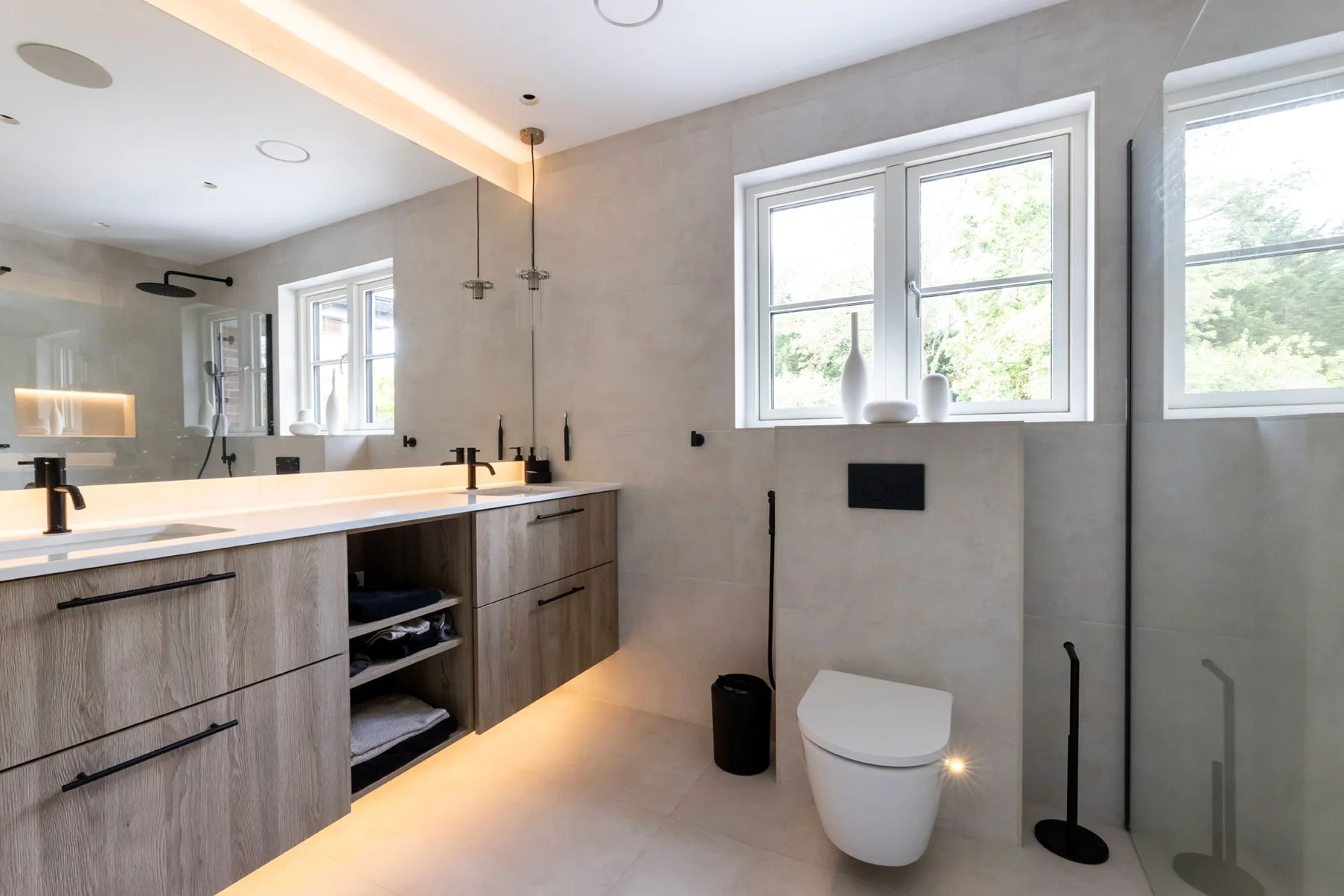 Modern bathroom with dual vanity, black faucets, shower area, and large windows with white frames, decorated with white vases and natural light.