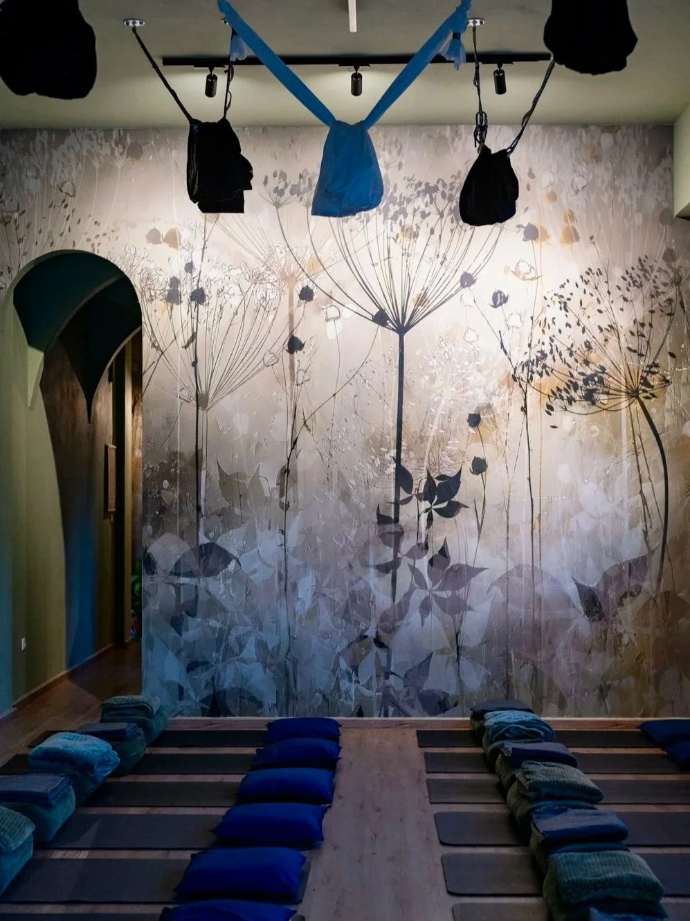 Yoga or meditation room with mats and cushions on the floor, a floral wallpaper mural, and hanging hand weights or bags from the ceiling.