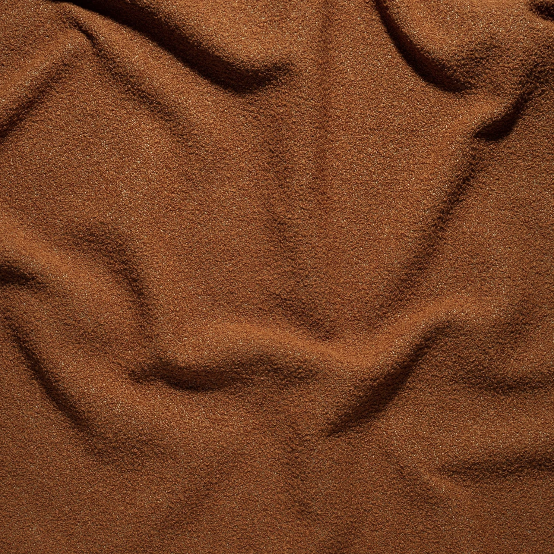 Close-up of brown fabric with a textured, granular surface and visible folds.