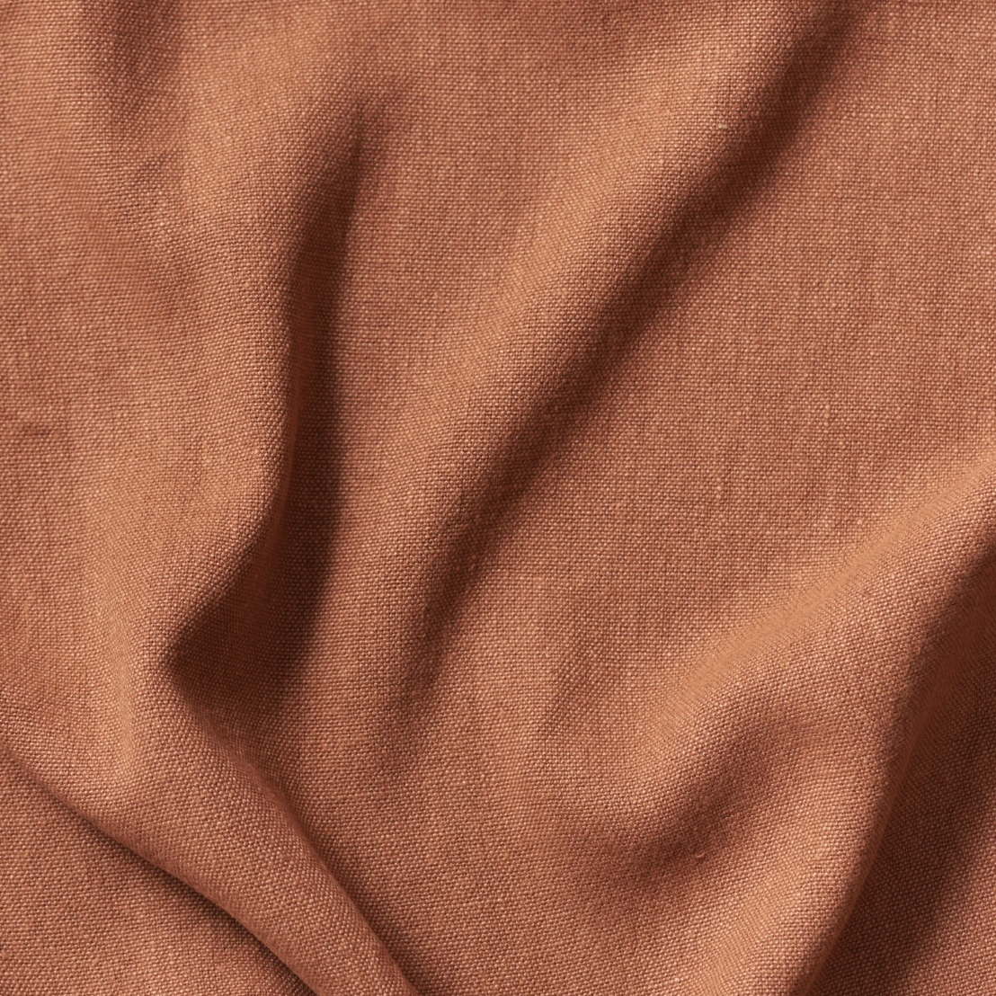 Close-up of a textured, rust-colored fabric with gentle folds.