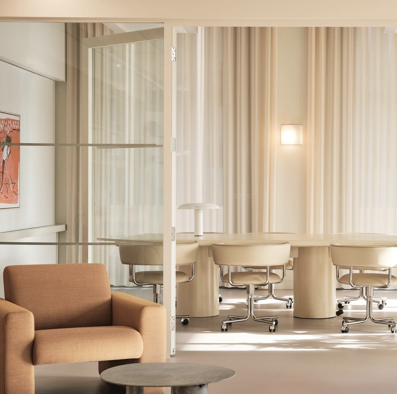 A minimalist living area with a peach-colored sofa, a round gray coffee table, and a background room with cream-colored chairs, a white lamp, and cream curtains.