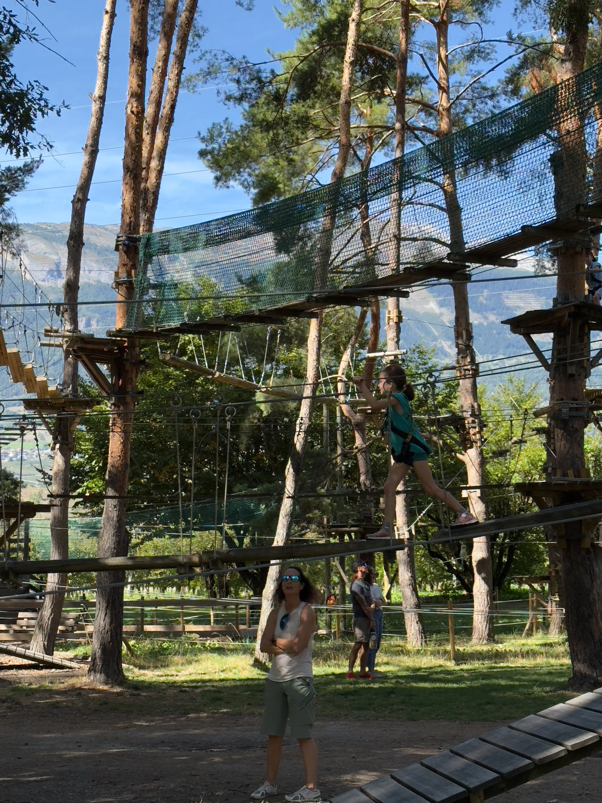 Une femme et deux enfants au Parc Aventures du Domaine des Îles. Accrobranches à Sion. Arbres, ponts suspendus en bois et des cordes.