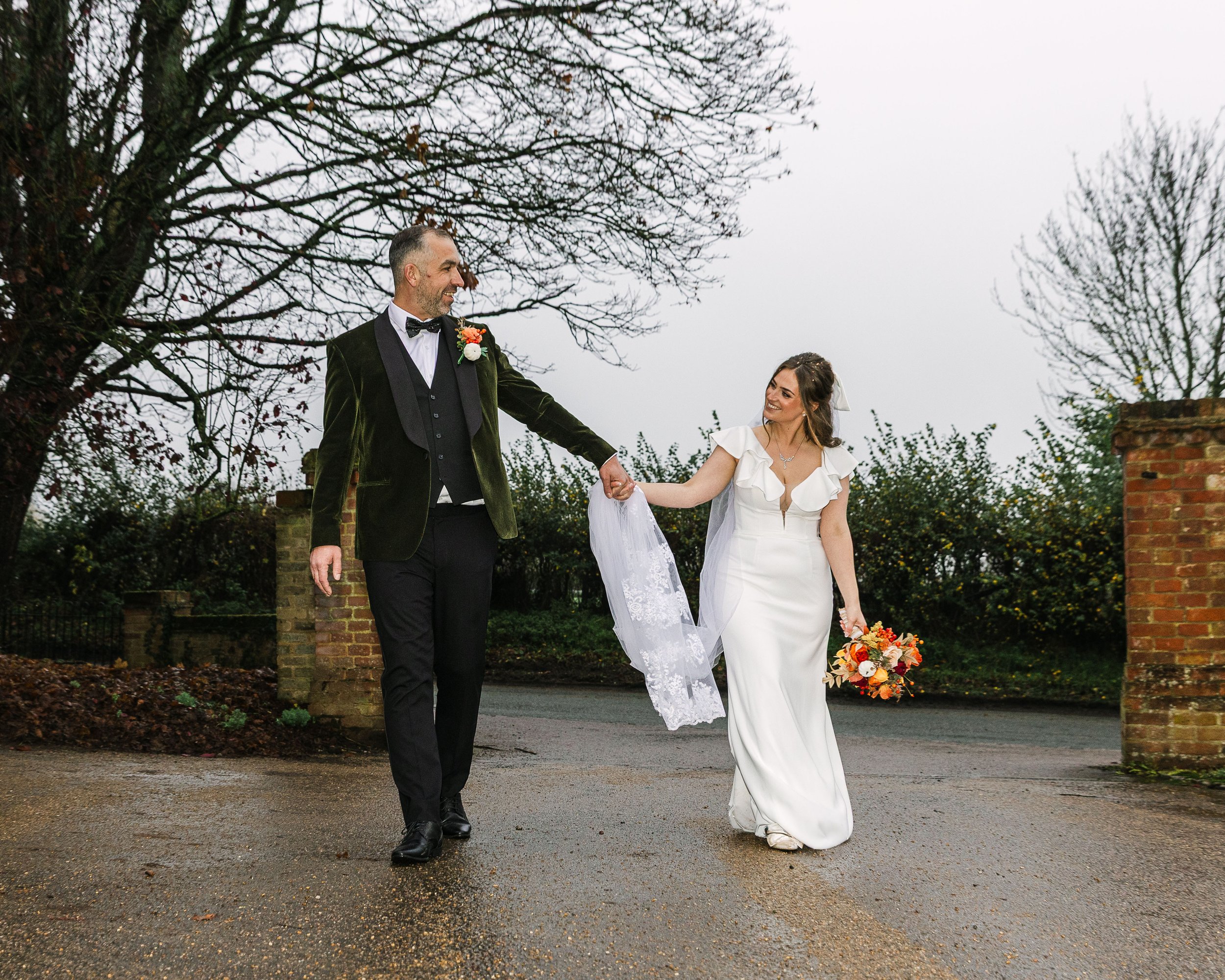 Bride and Groom holding hands at their autumn wedding in Bedfordshire. Groom is wearing a velvet green tux and the bride has on an ivory plunge wedding dress with frills around the sleeves and neckline
