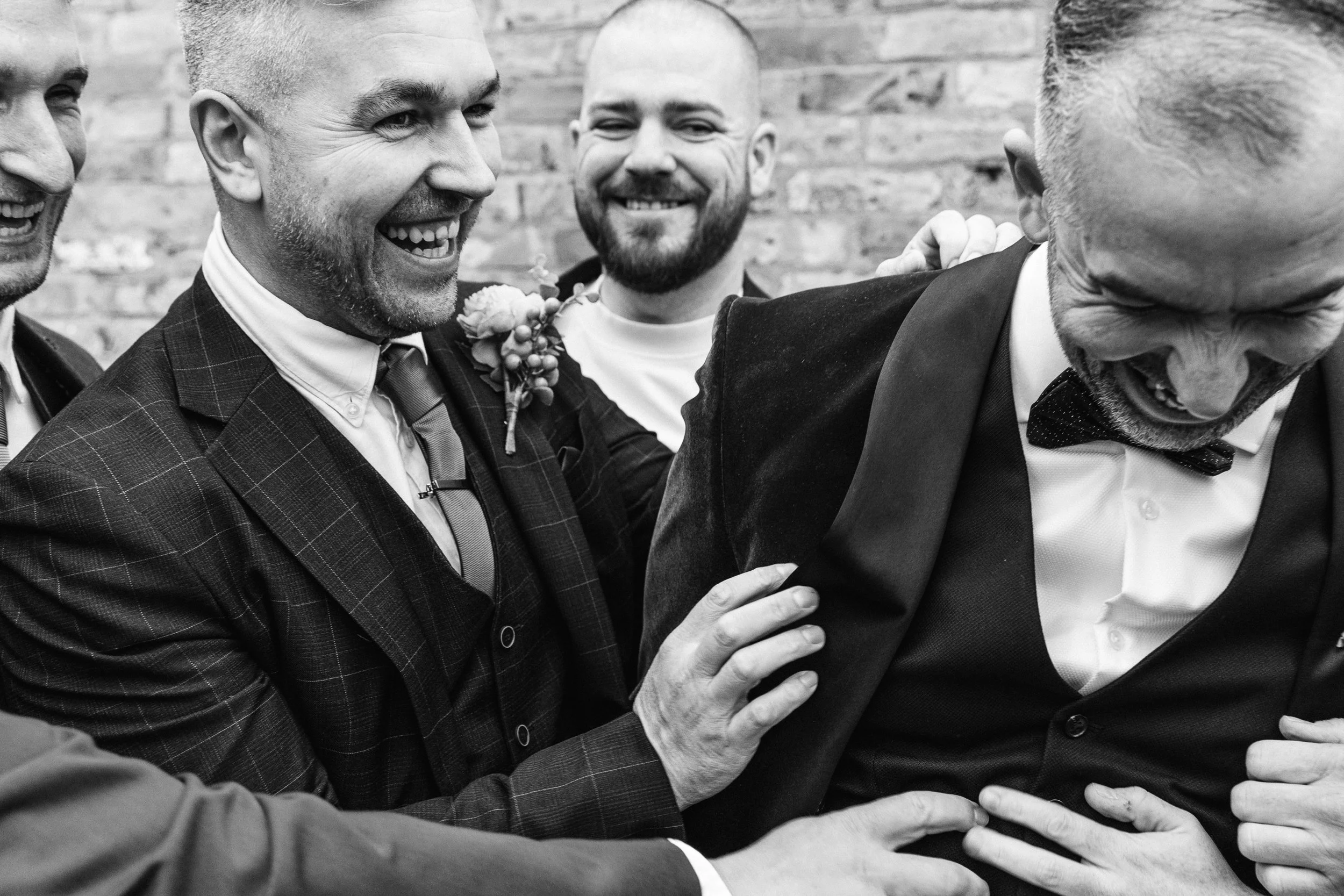 Close up shot of a smiling groom at his Bedfordshire wedding surrounded by smiling groomsmen up in suits