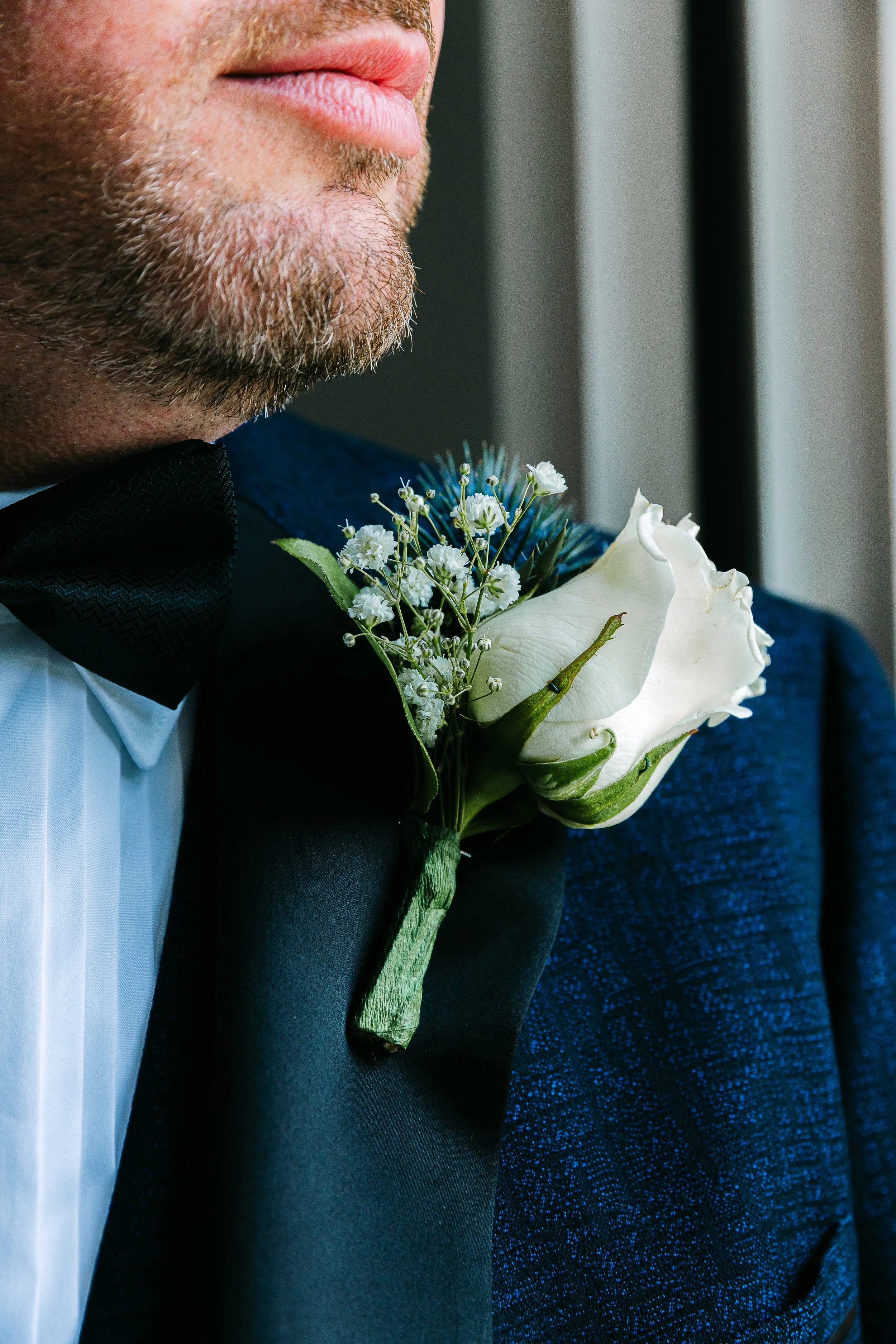 Close up shot of a grooms button hole flower which is white against the navy blue of his suit jacket