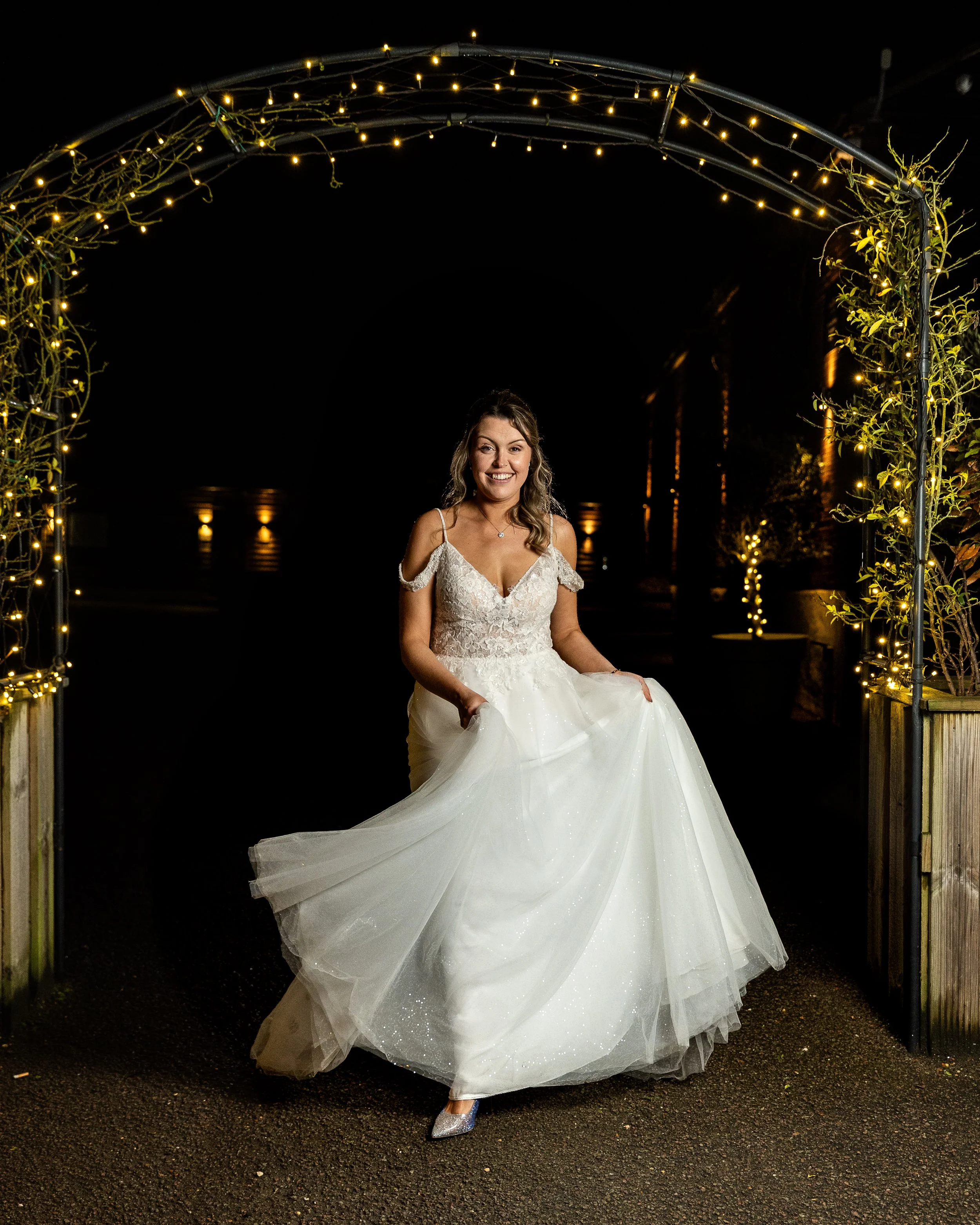 Bride in a sparkly wedding dress under Christmas lights at her winter wedding in Hertfordshire