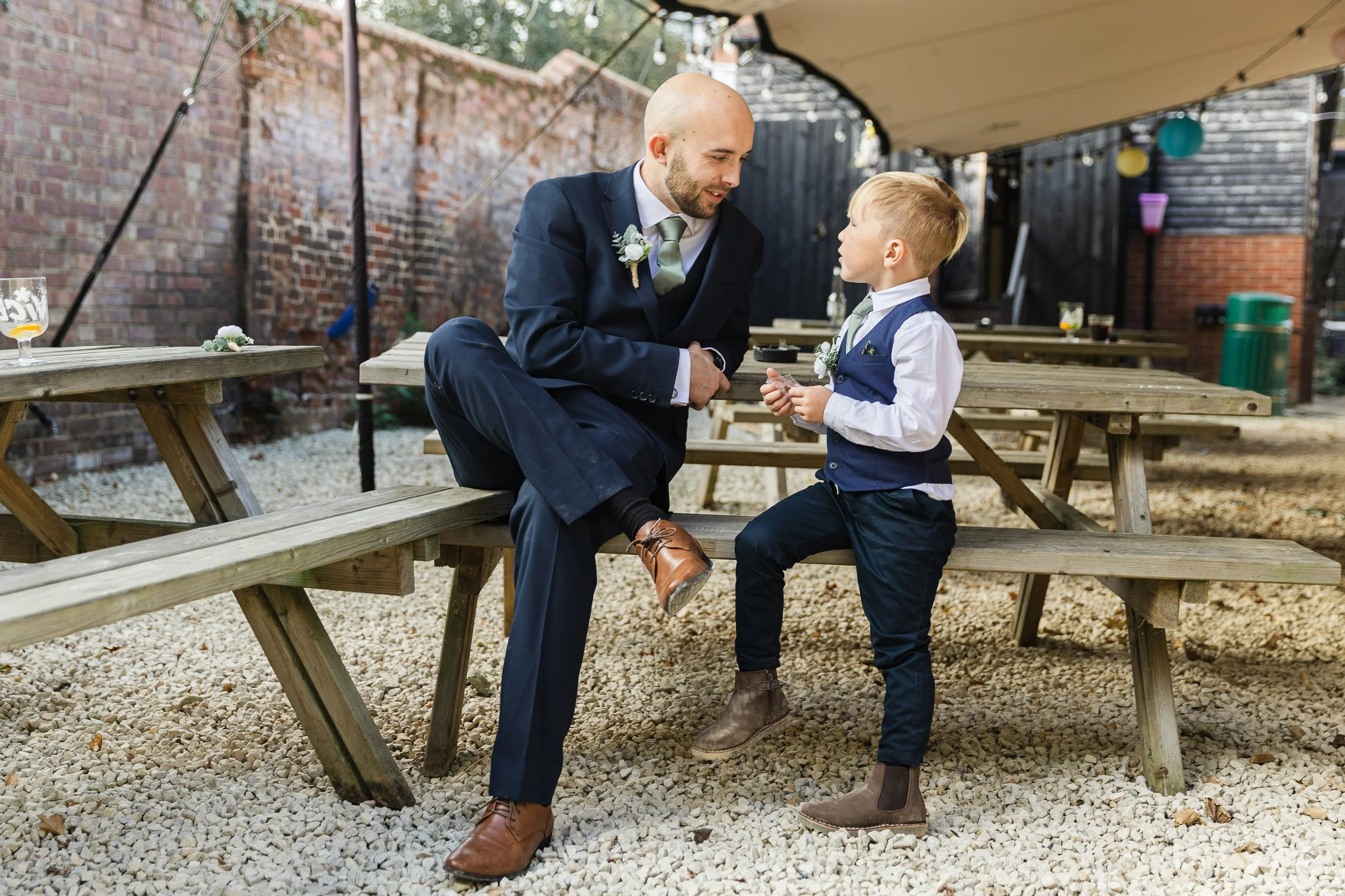 Groomsmen and his young nephew sitting facing each other on a bench at a wedding in Ampthill Bedfordshire
