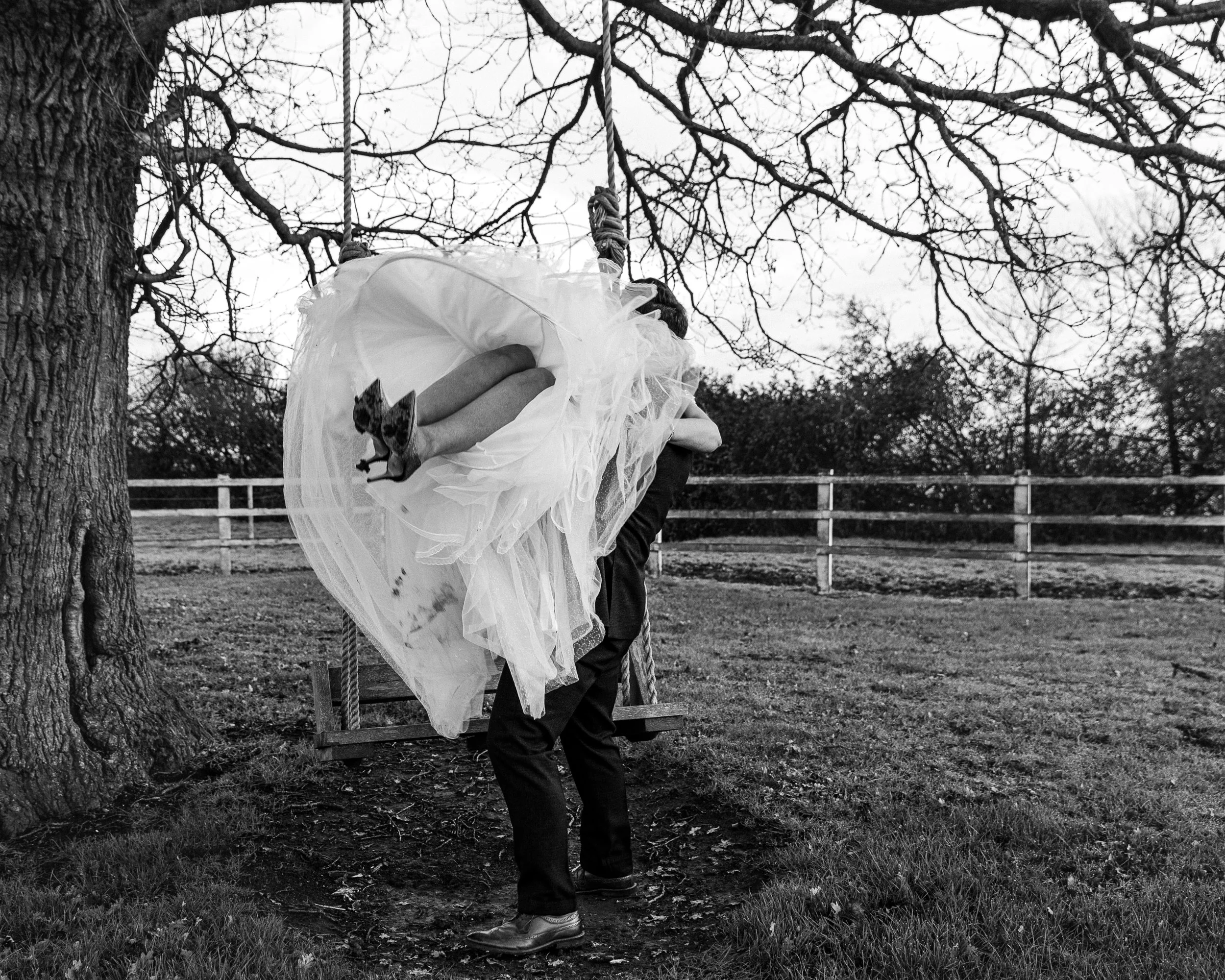 Groom carries his bride to a swing showing just her legs under her wedding dress at a Hertfordshire wedding venue