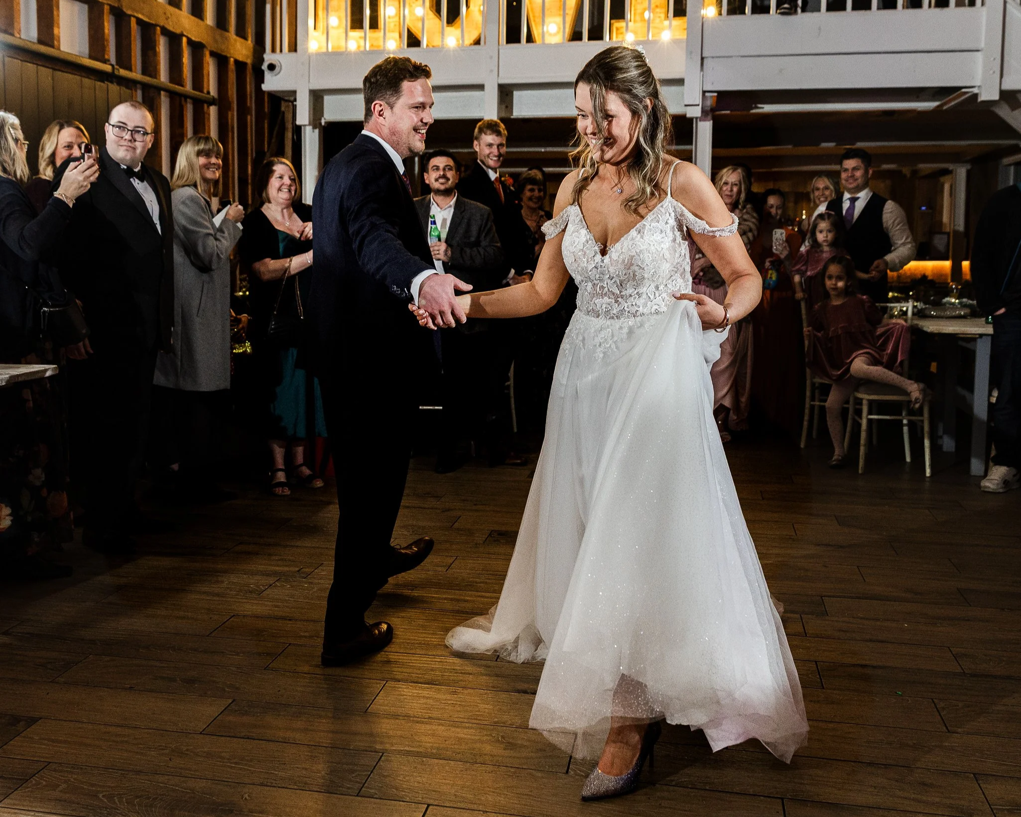 A bride and groom dance at their wedding reception with guests watching and smiling in the background.