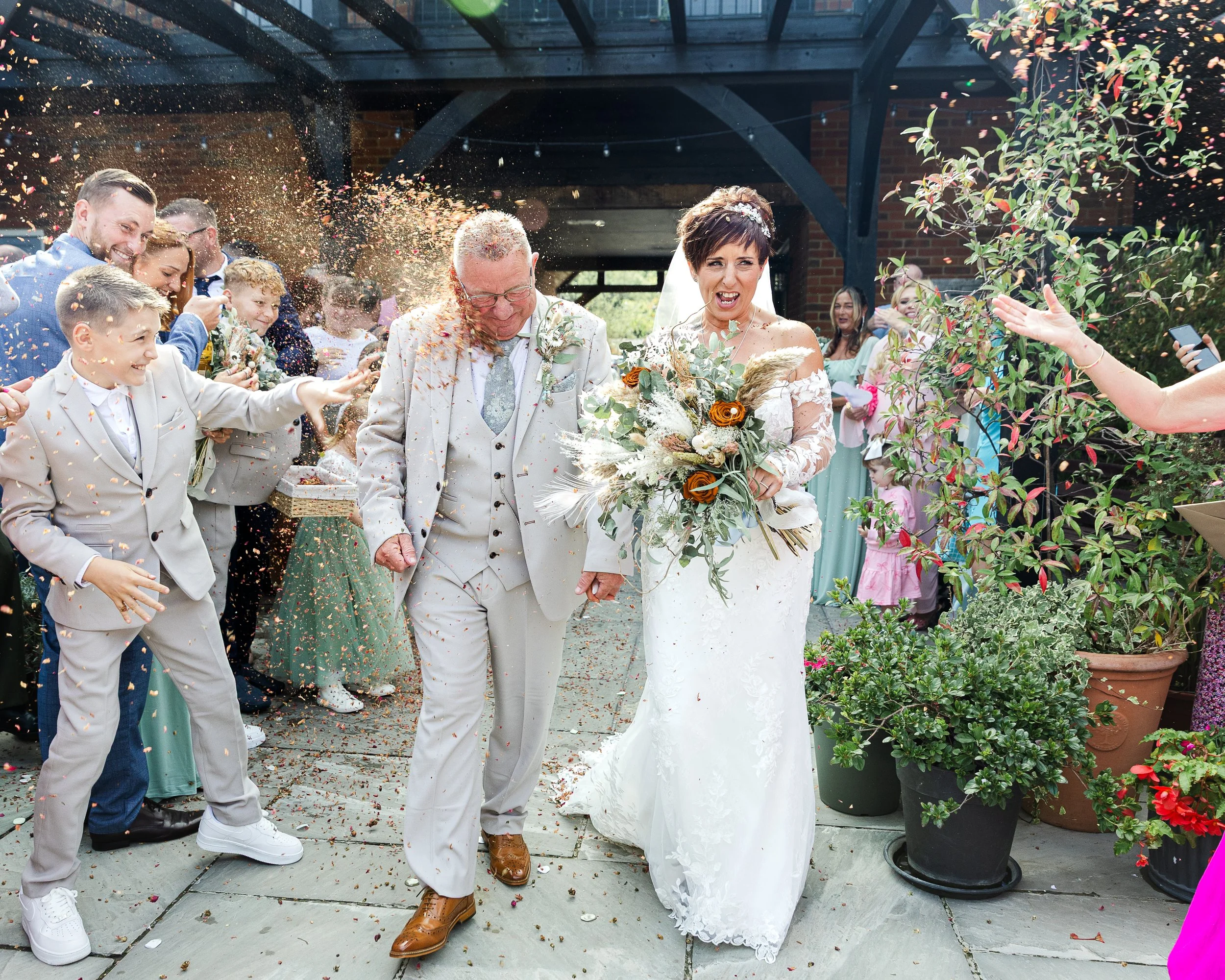 Bride and Groom walking down a confetti line on their wedding day with the groom being hit by a large amount of confetti