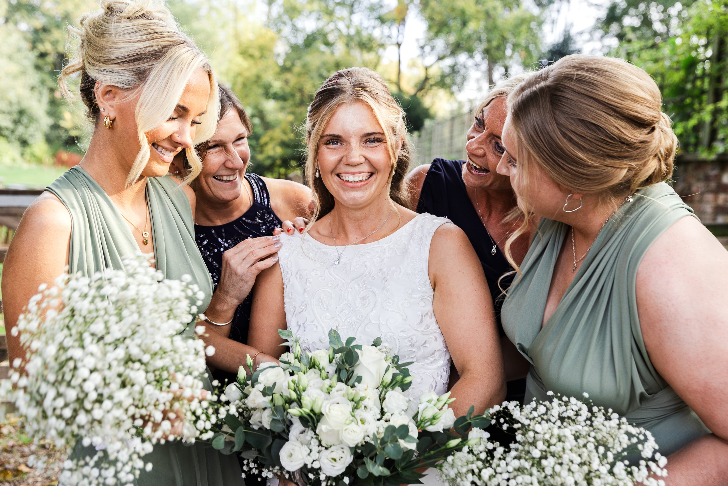 A bride in an ivory embroidered wedding dress surrounded by her bridesmaids and two women. All looking on at her whilst holding their bouquets to the front of the image. Taken at the White Hart Ampthill