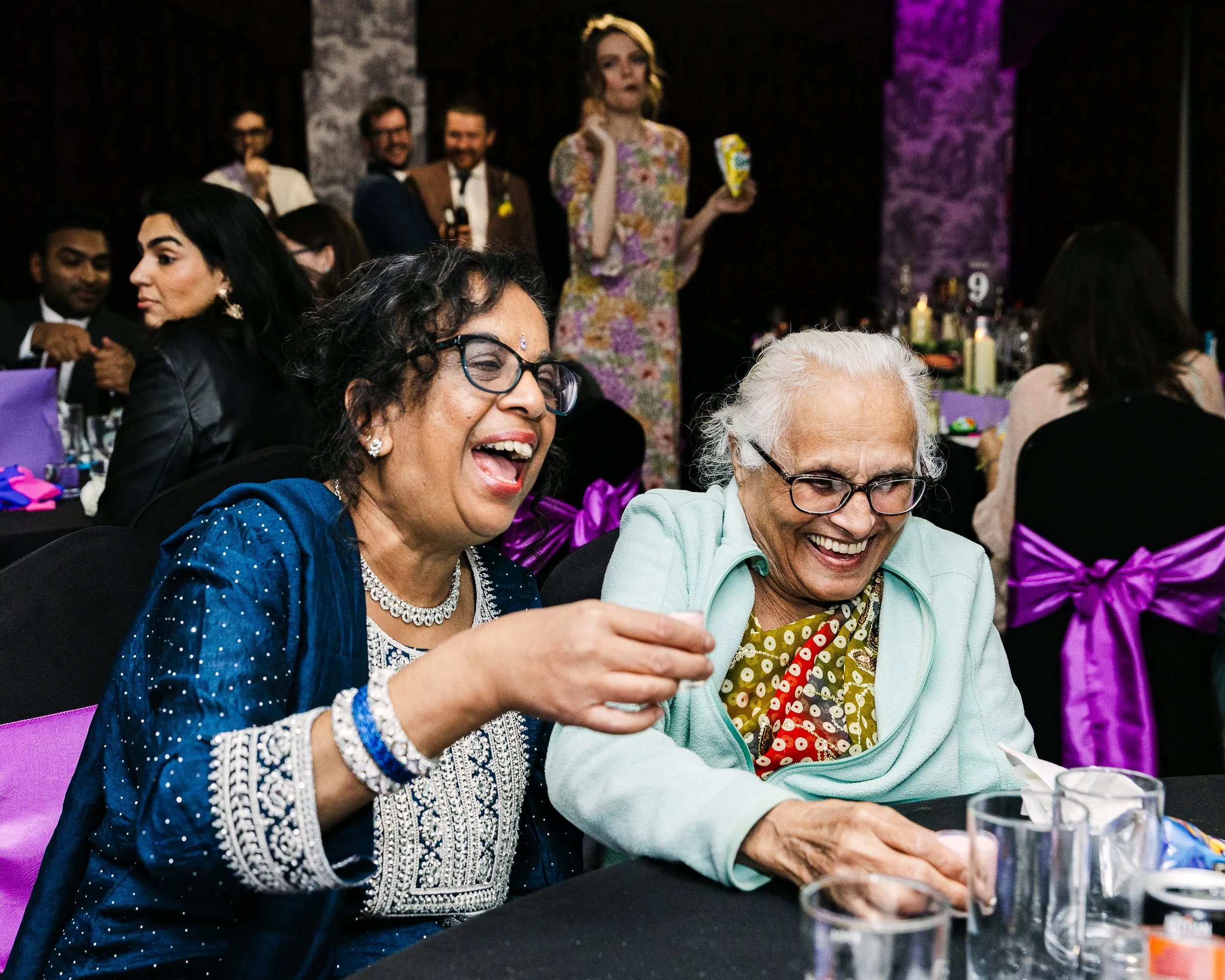Two ladies sitting side by side laughing hysterically at an Asian-Anglo fusion wedding in Buckinghamshire