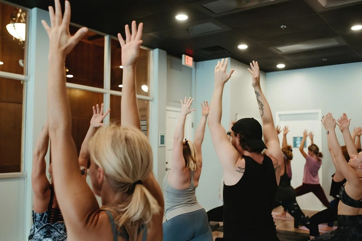 Students with arms raised in Warrior One during a vinyasa yoga class