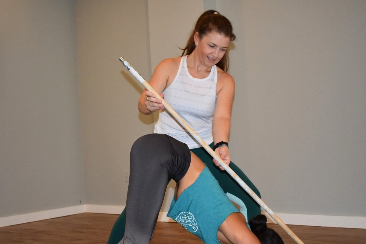 Doctor of Physical Therapy using a stick to assess a student's yoga alignment for safety
