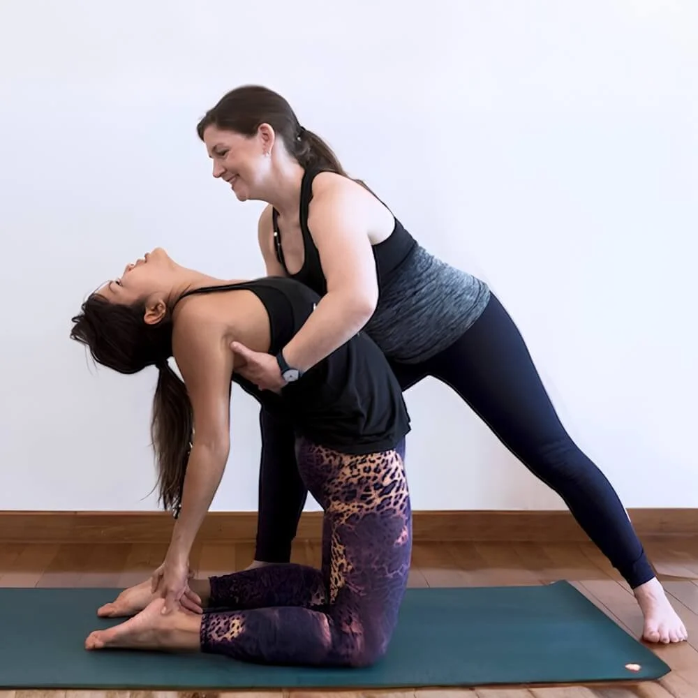 Dr. Trish Corley assisting a student in camel pose during a private yoga session on the Estoril Coast