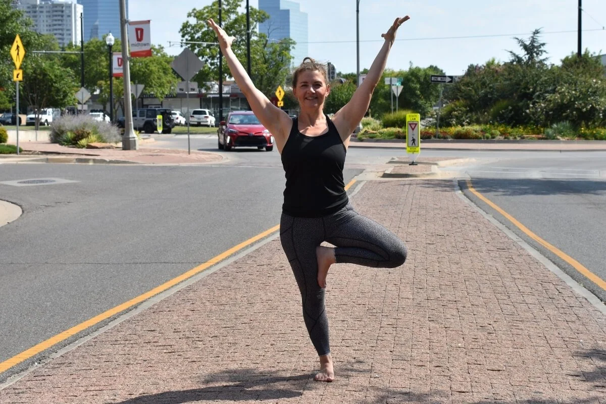 Dr. Trish Corley in tree posture outdoors, demonstrating how yoga foundation cues create balance through the standing foot