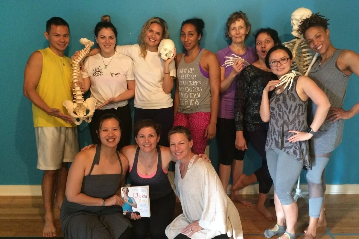 Dr. Trish Corley holding a book on chakras with students in an advanced yoga anatomy teacher training