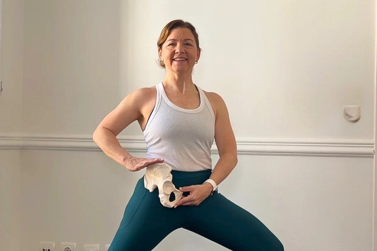 Dr Trish Corley holding bones and demonstrating neutral pelvis in warrior two
