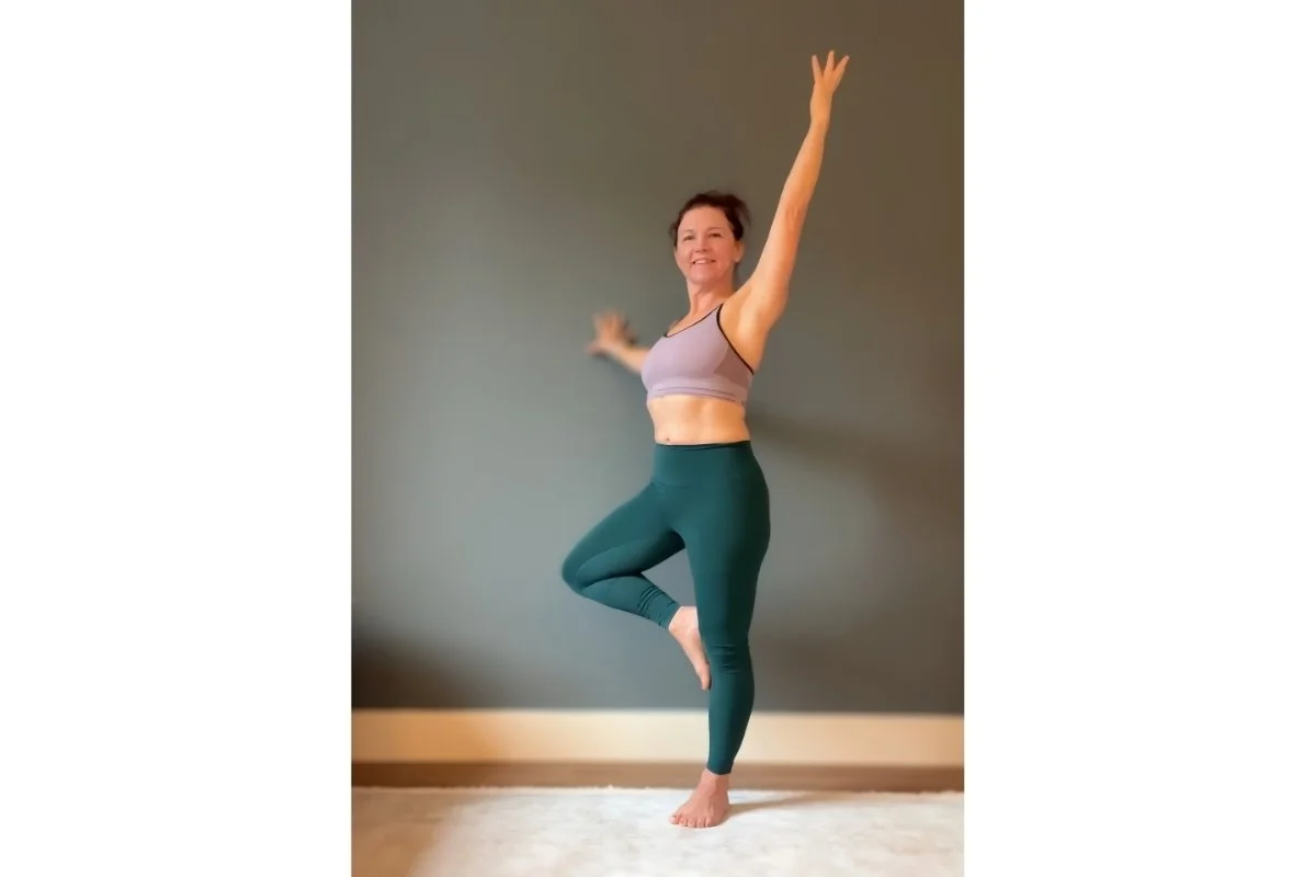 Trish Corley in tree posture with one hand touching a wall, expanding the base of support for balance