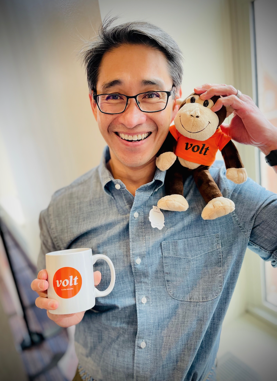 Headshot of Voltaire Santos Miran holding a volt-branded stuffed monkey in one hand and a volt-branded coffee mug in the other.