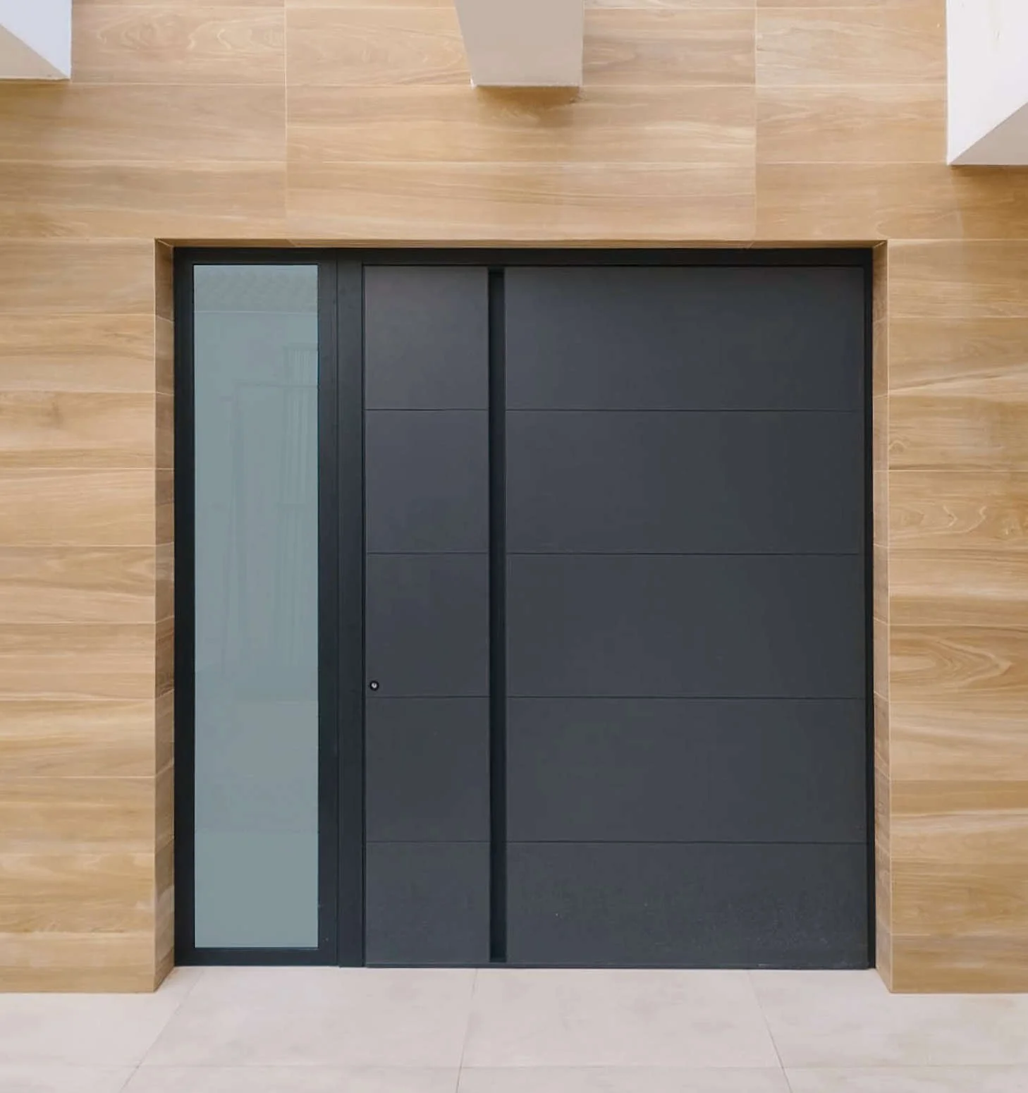Puerta moderna negra con marco de metal, junto a pared de madera y pared blanca, en un entorno interior.