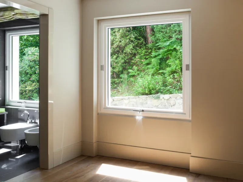 Vista de una habitación con una ventana grande que muestra un paisaje natural con árboles y vegetación verde.