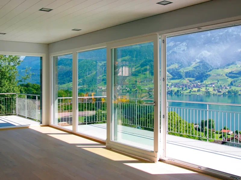 Sala con grandes ventanales que ofrecen vista panorámica de montañas, un lago y un valle con casas y árboles.