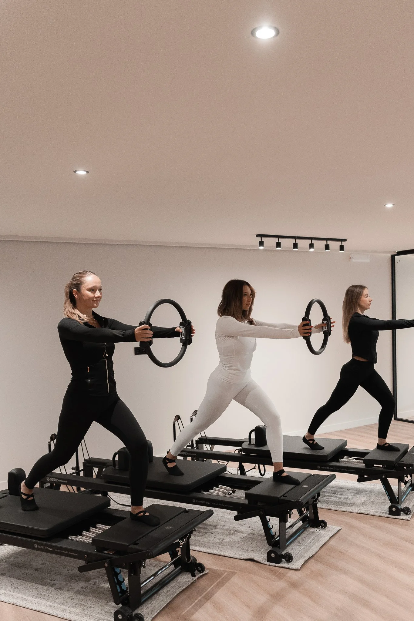 Trois femmes faisant du fitness sur des appareils de Pilates ou de rééducation, dans une salle propre et bien éclairée.
