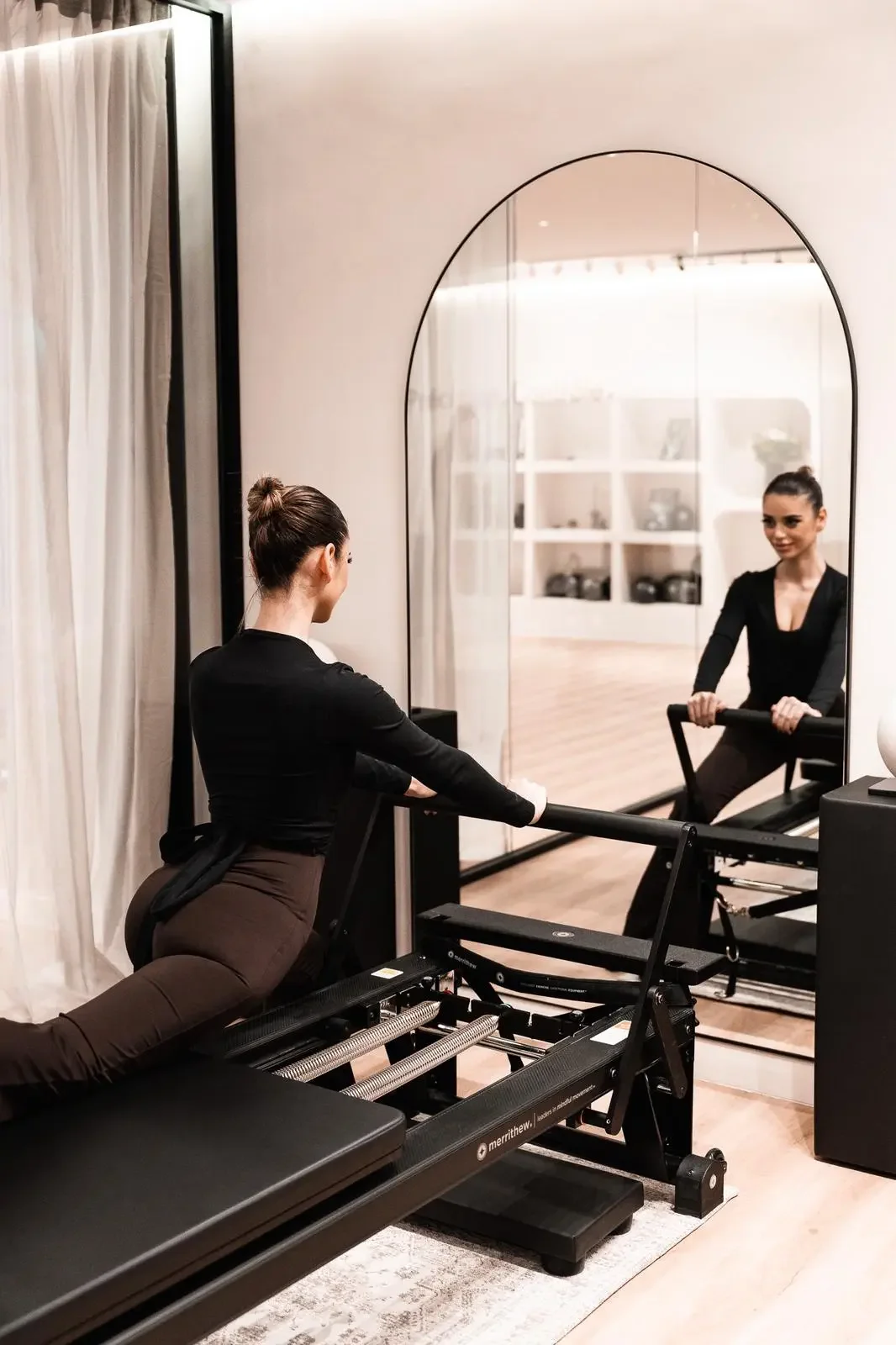Une femme faisant du fitness sur un appareil de Pilates ou de rééducation, dans une salle propre et bien éclairée.
