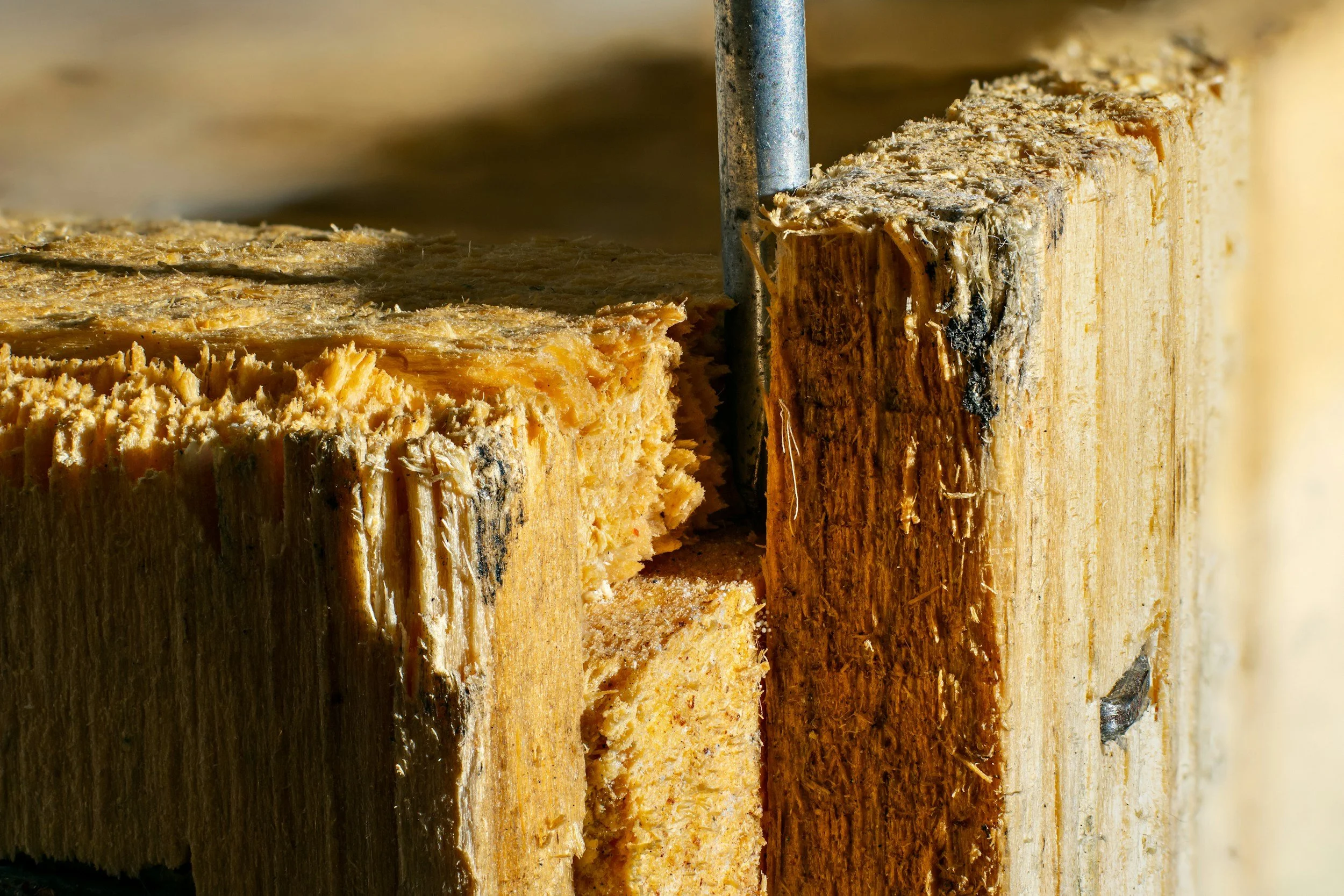 Close-up of a wooden post with a nail and a chipped section, showing the rough texture and grain of the wood.