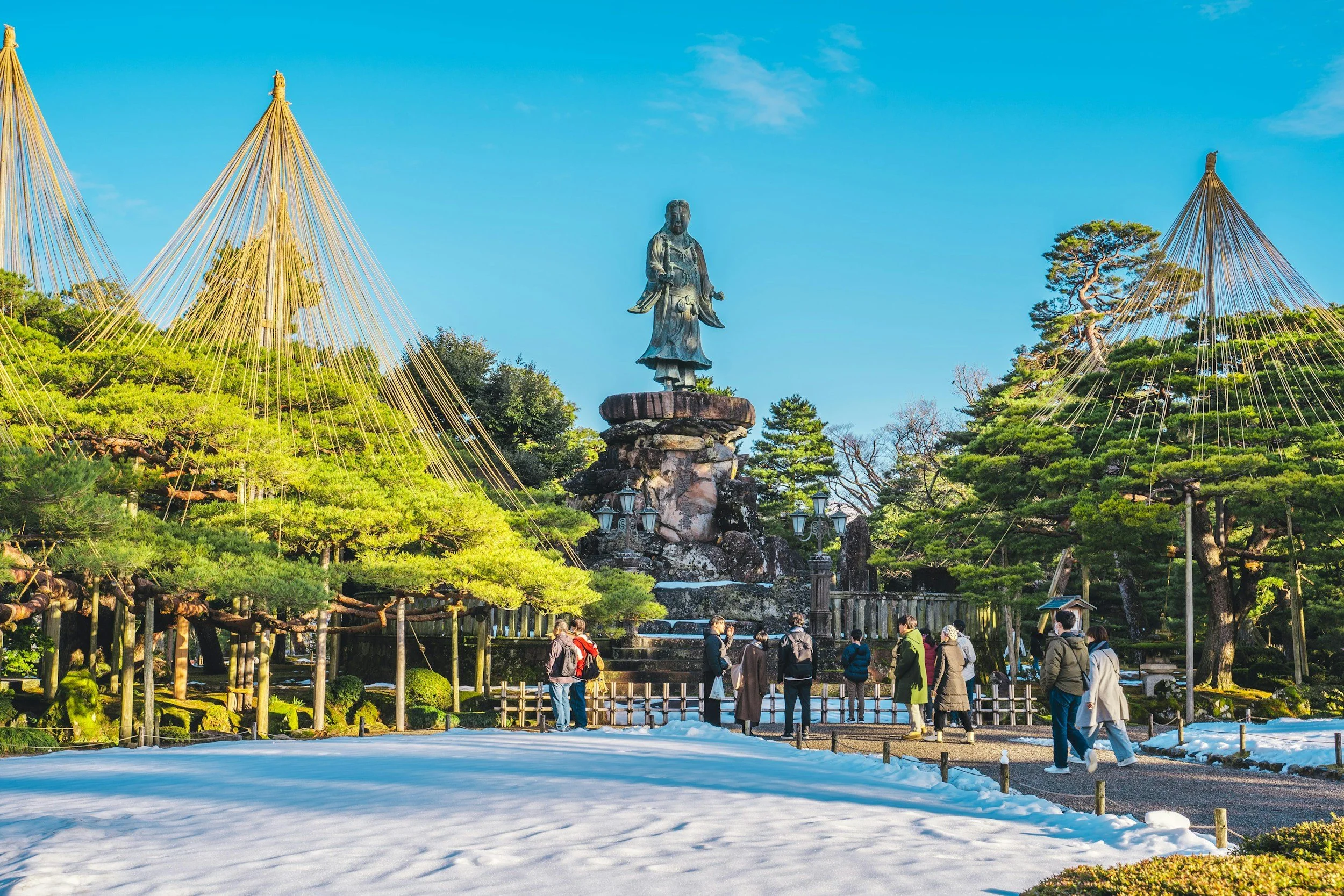 Visiteurs dans un jardin japonais avec grande statue, balade culturelle au Japon.