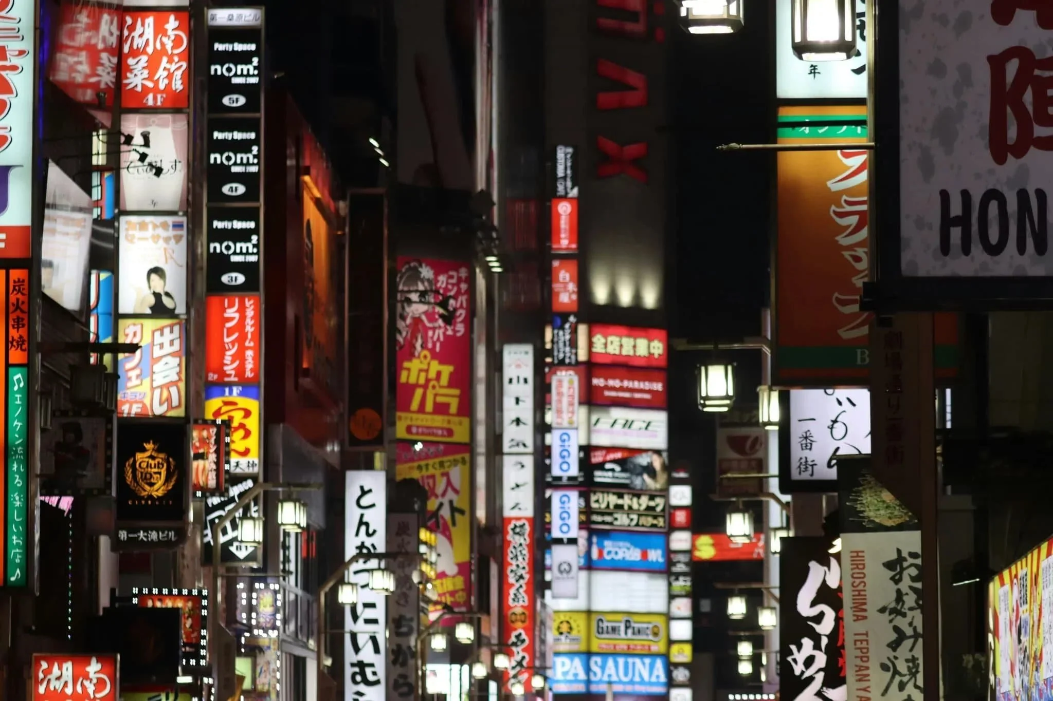 Rue de Tokyo avec enseignes lumineuses et restaurants, quartier animé de nuit.