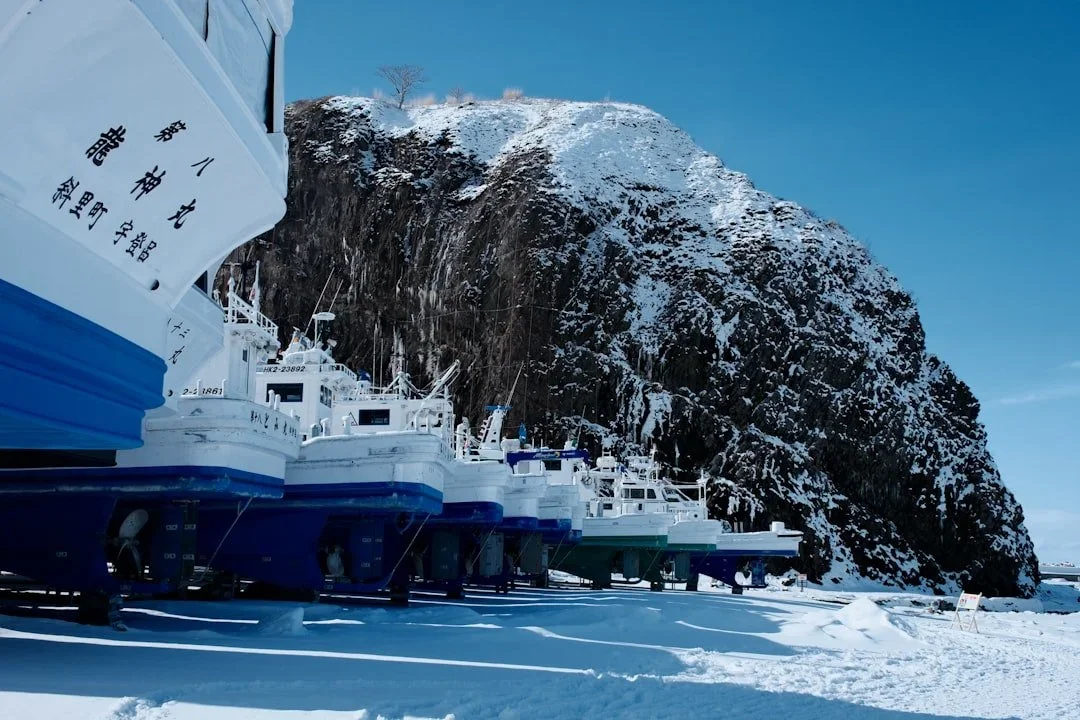 Bateaux de pêche au repos dans la neige, falaise enneigée en arrière-plan, hiver au Japon.