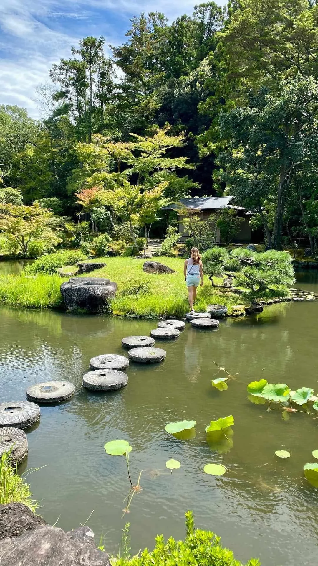 Claire traverse un petit pont de pierre dans un jardin japonais, balade zen au Japon.