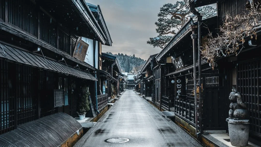 Rue calme dans un village traditionnel japonais, maisons en bois noir et montagnes.
