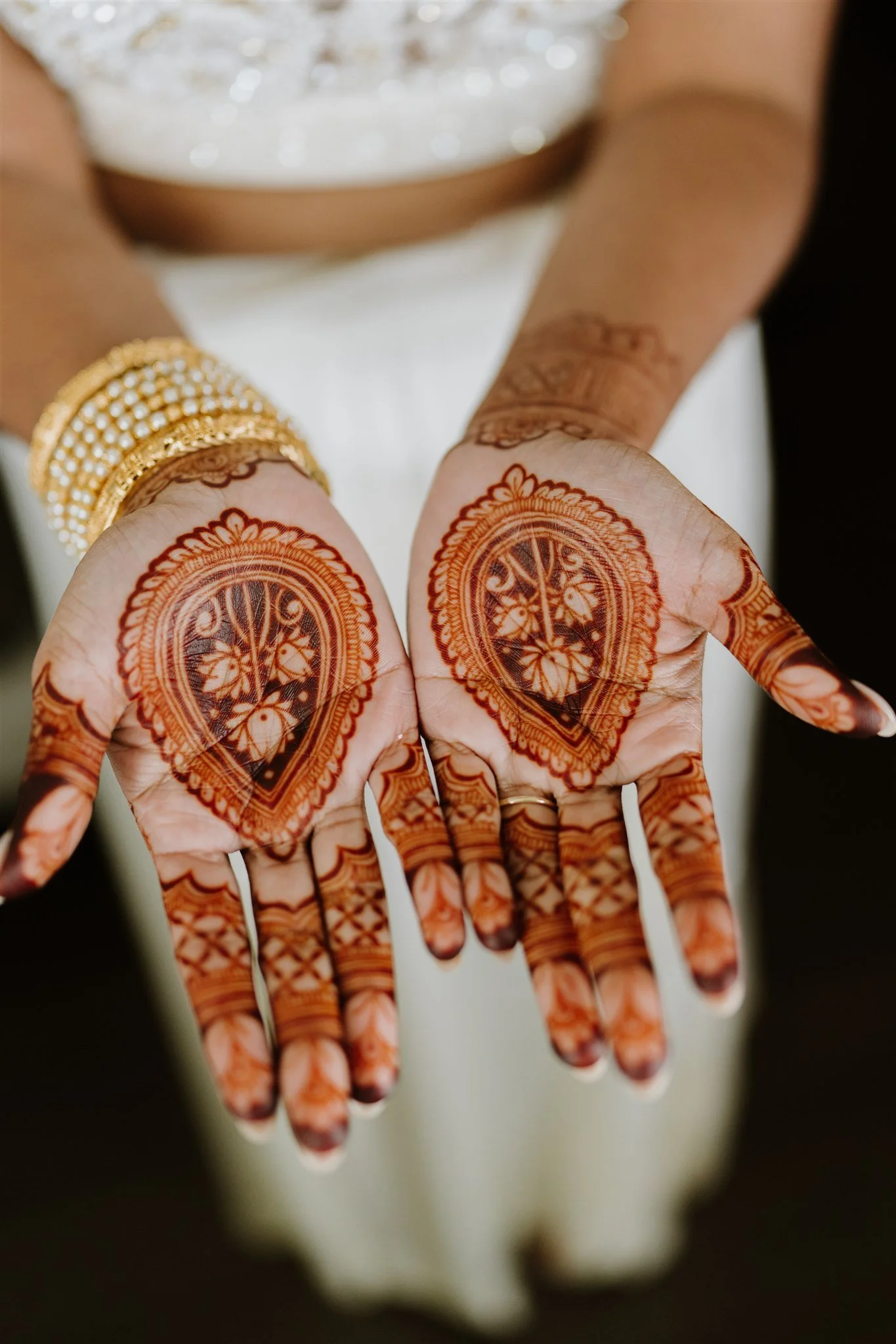 Close-up of hands with intricate henna designs and gold bangles, celebrating a wedding