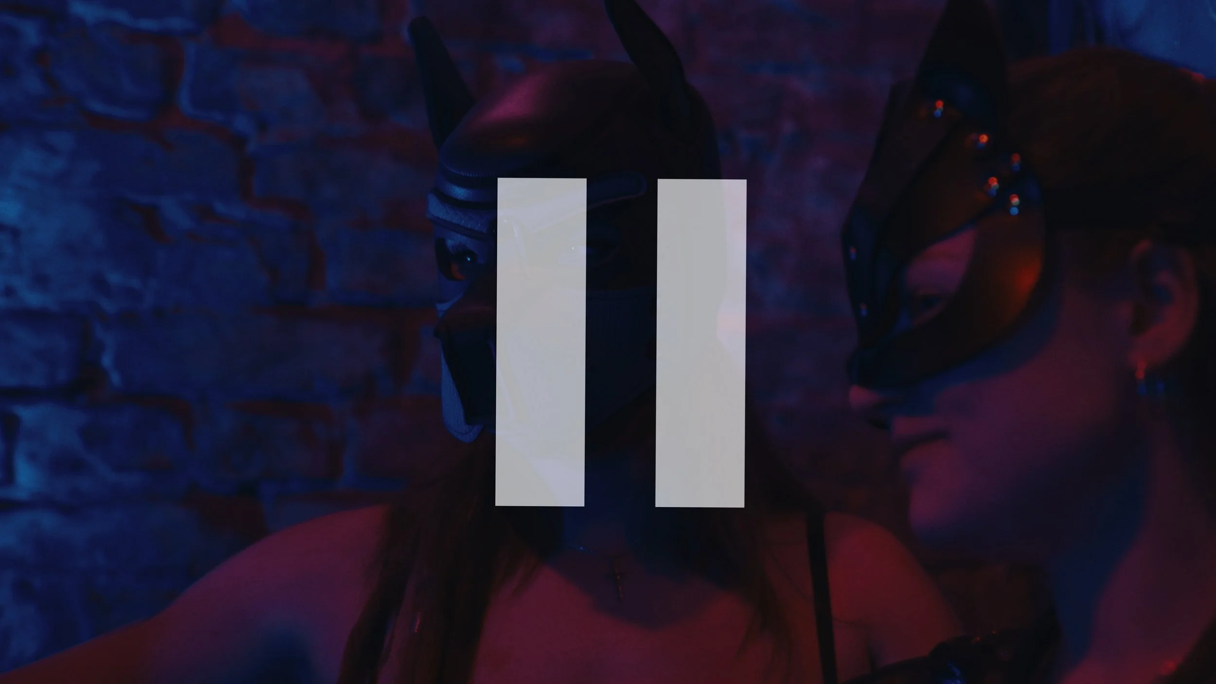 Donna con maschera da gatto in un ambiente con luci blu e rosse, sfondo di muro di mattoni.