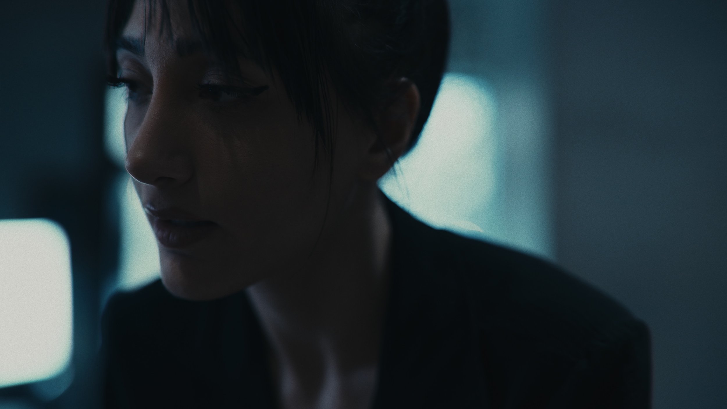 Ragazza con capelli corti e scuri in un'illuminazione soffusa, volto parzialmente in ombra, ambientazione moderna e minimalista.