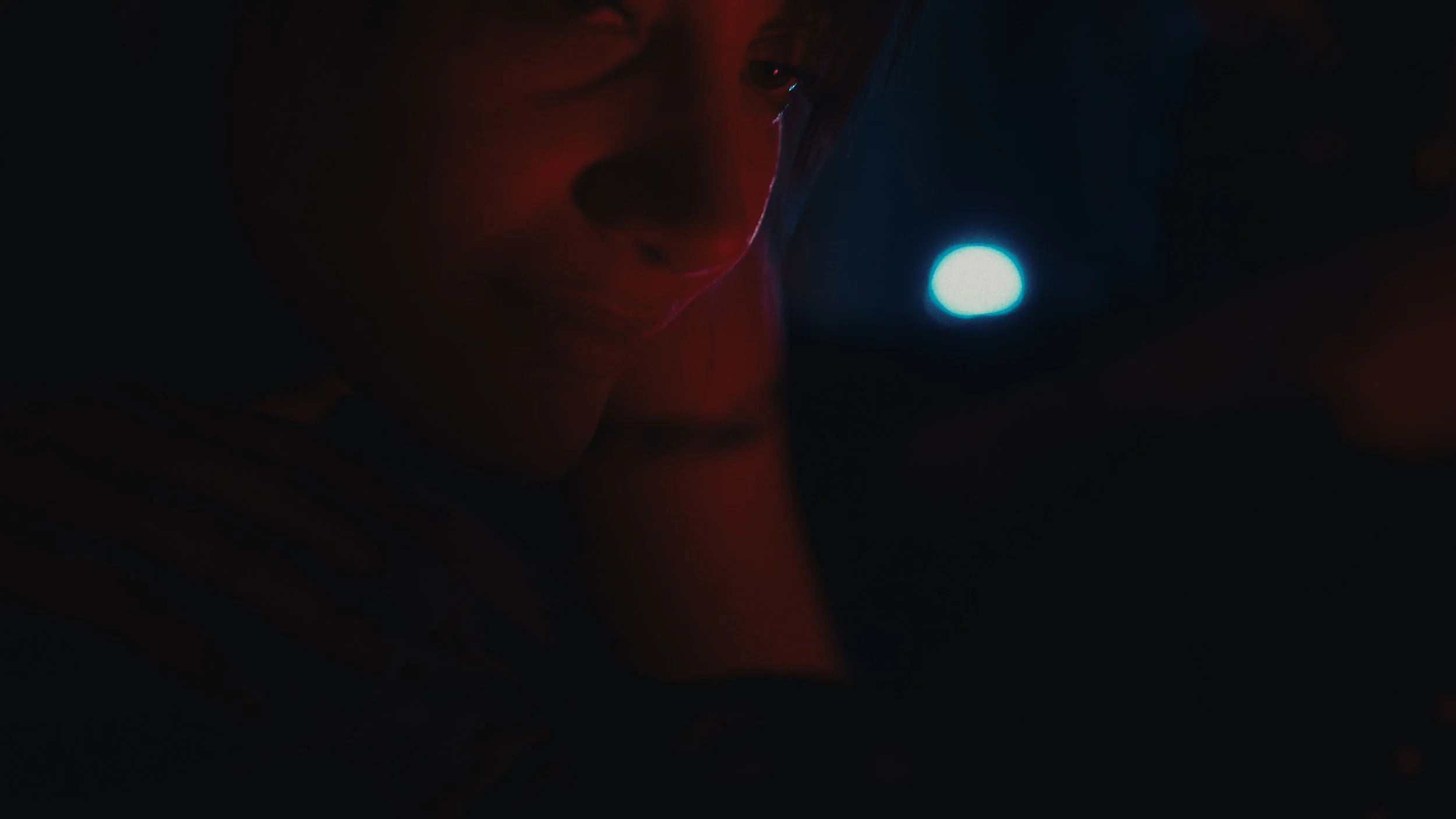 Una persona con un casco e una visiera, illuminata da una luce blu, in un ambiente scuro.