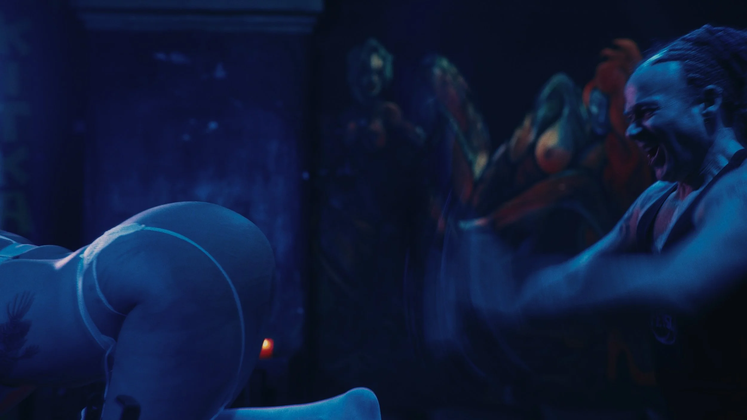 Una persona che sorride e ride con entusiasmo in uno spazio oscuro, con un murale colorato sul retro.