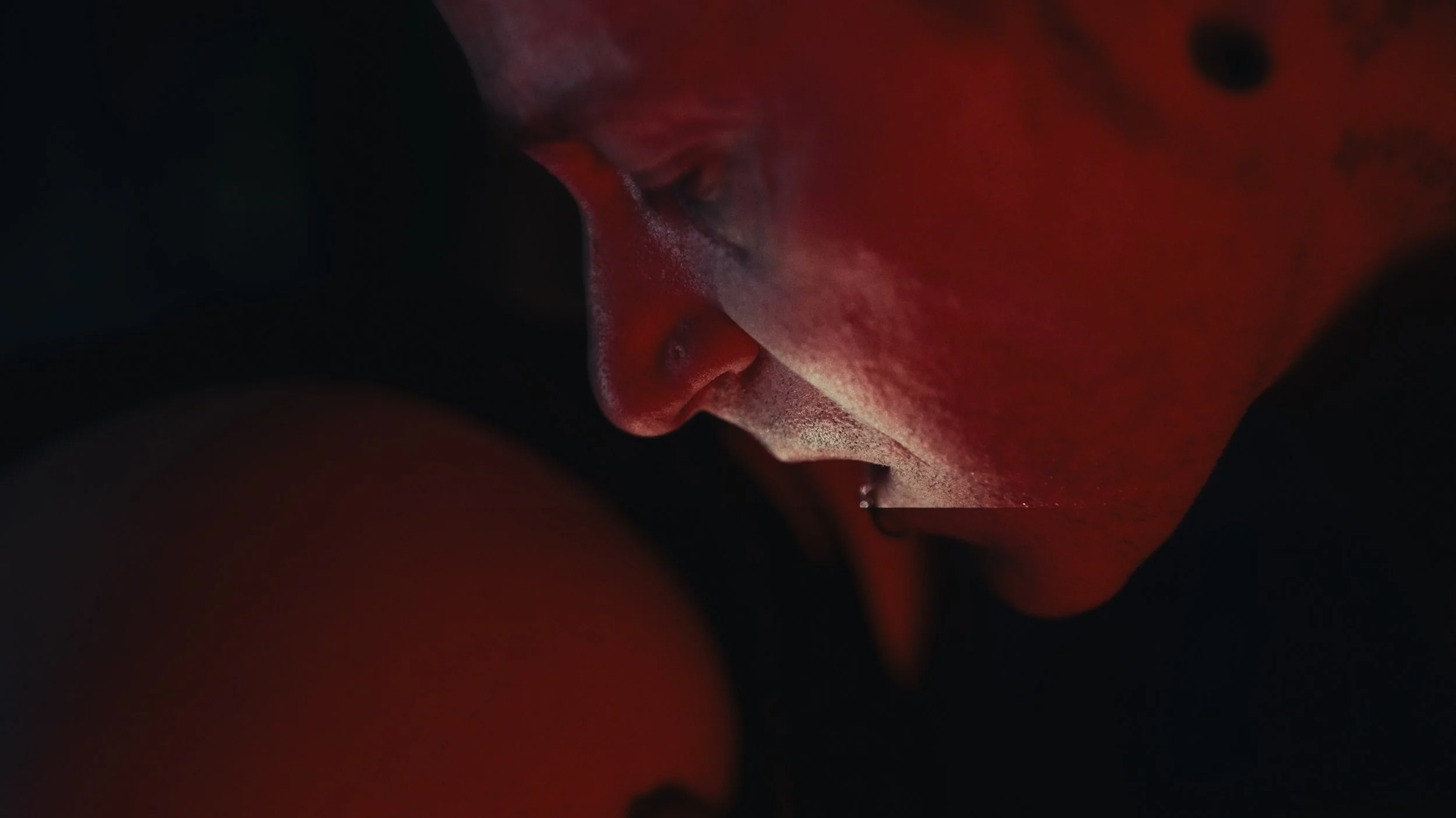 Primo piano di un volto umano in un ambiente buio con illuminazione rossa, vista laterale e con occhi chiusi