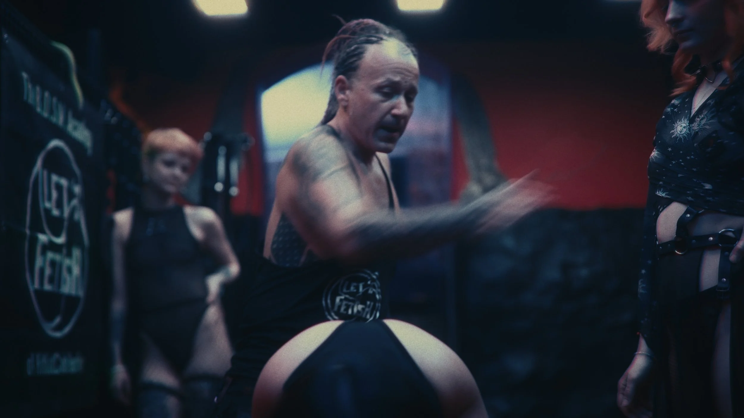 Una donna trasandata in una palestra di lap dance fa stretching tra donne con abiti ristretti e tatuaggi