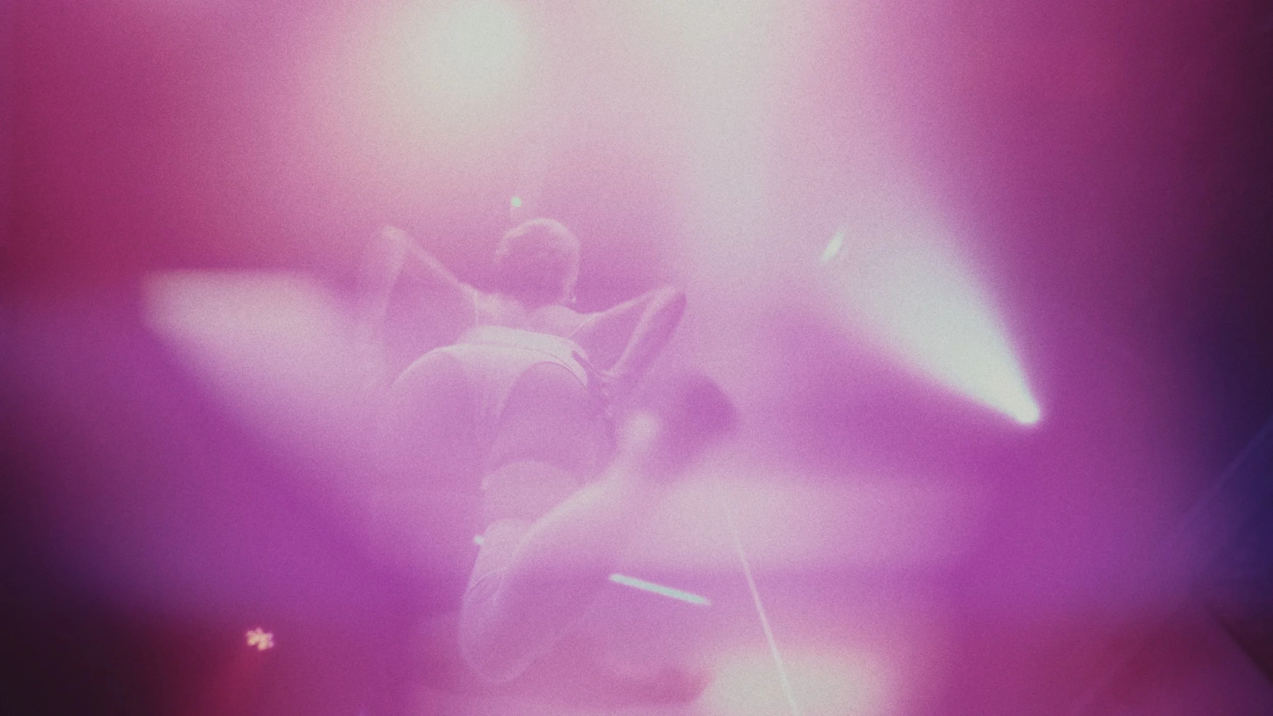 Due ballerini in scena sotto luci rosa e viola, uno si trova in piedi mentre l'altro si trova in posizione di danza.