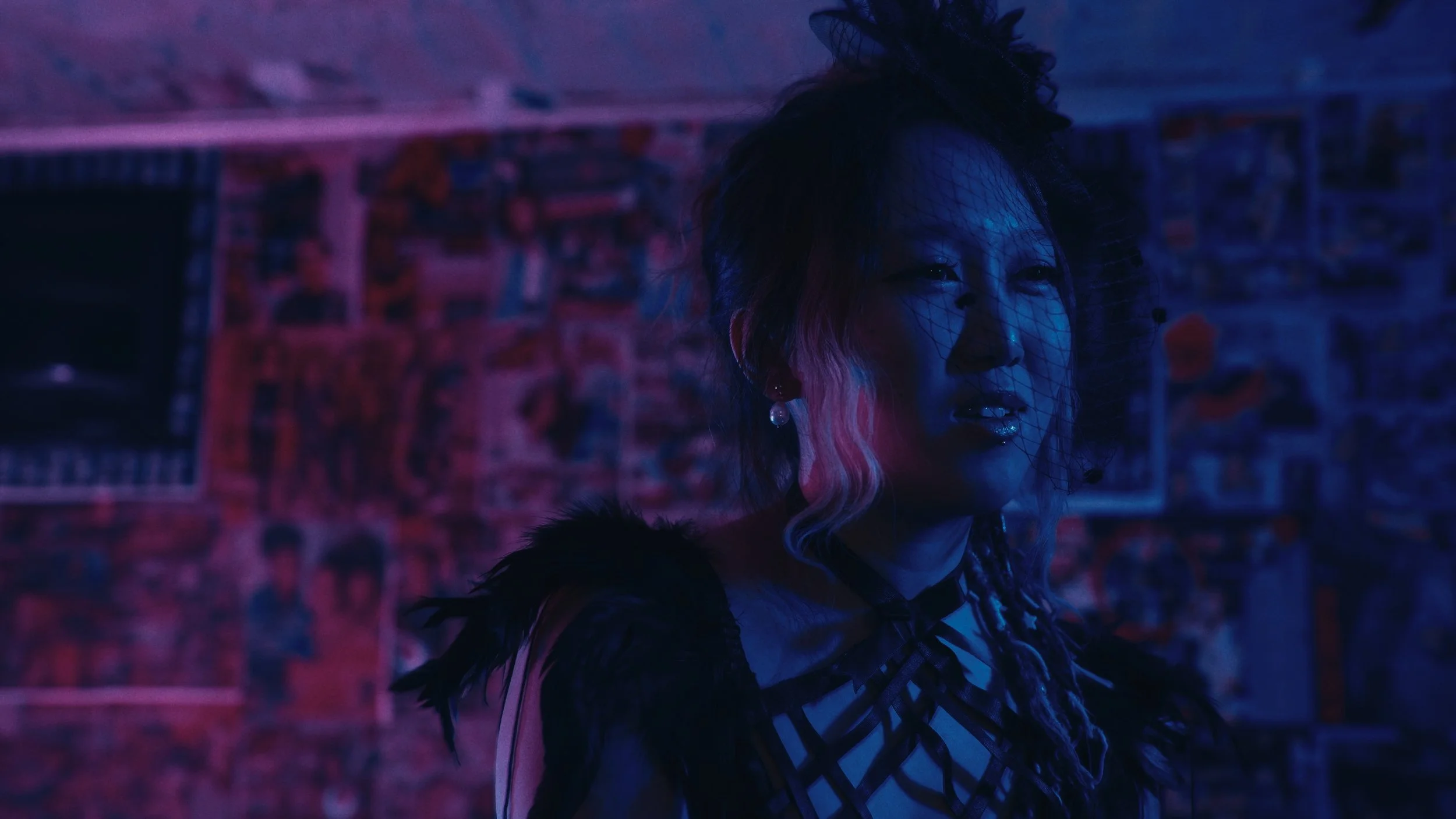 Ragazza con cappello di rete, trucco glitterato, abbigliamento alla moda, in un ambiente con luci soffuse di colore blu e rosa, sfondo con poster e graffiti.