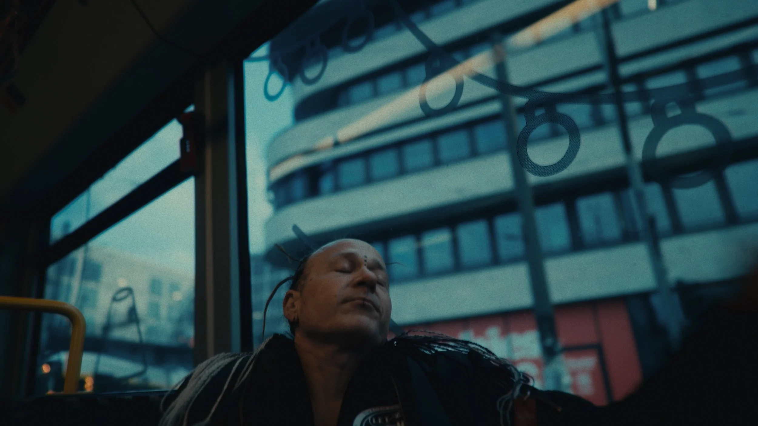 Persona che dorme su un autobus con finestra con riflessi di edifici moderni.