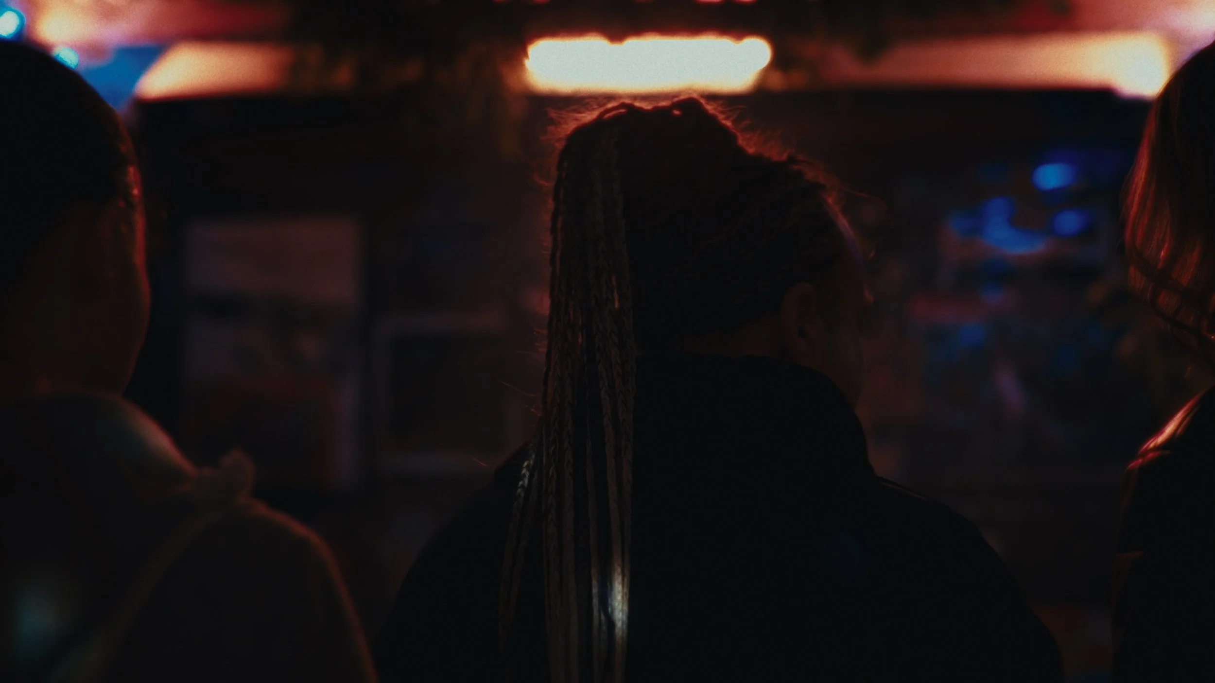 Sgabberi di persone sedute in un locale con luci soffuse di colore rosso e blu, con uno sfondo luminoso in alto.