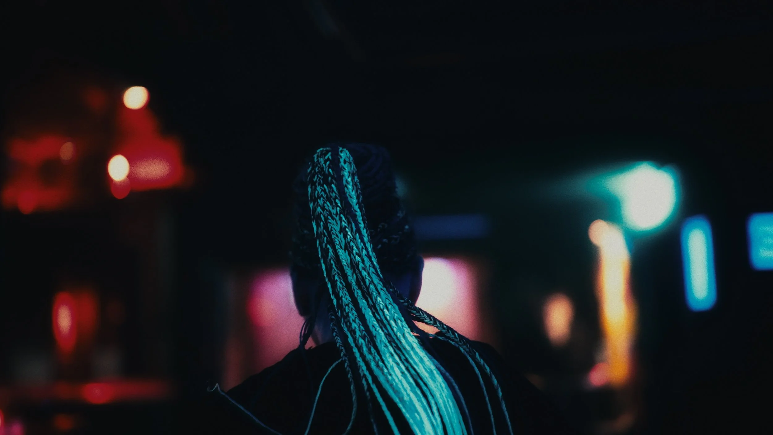 Una persona con treccine luminose bluastro in un ambiente scuro e con luci al neon colorate
